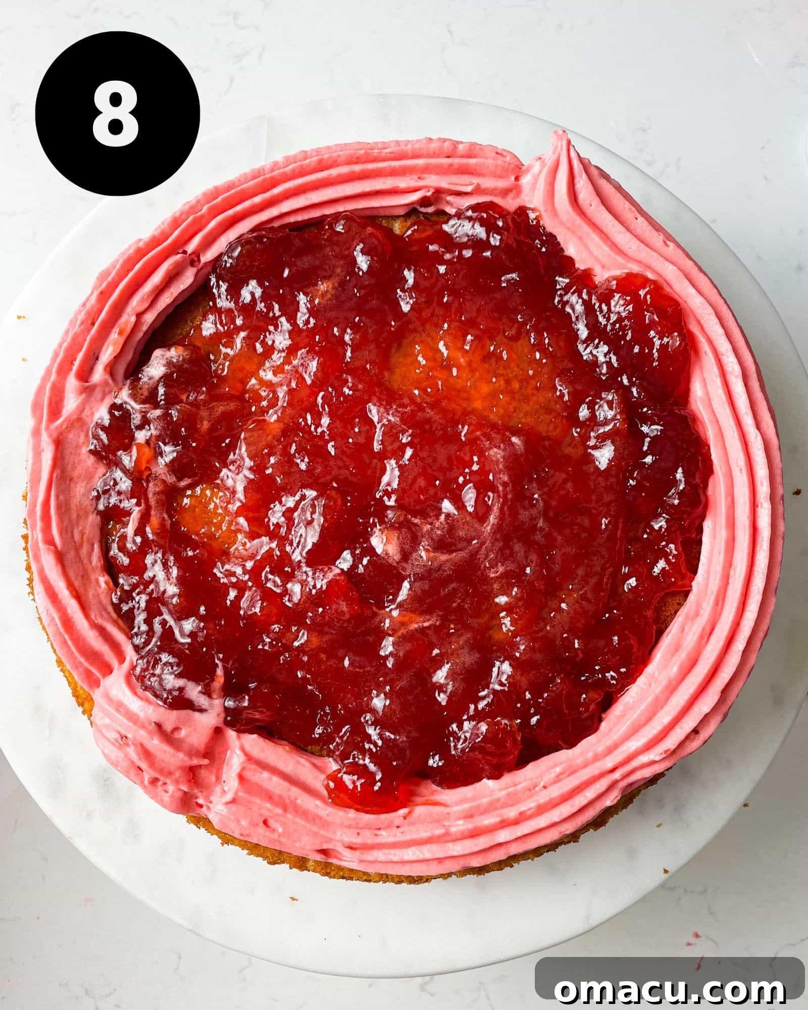 a cake layer with strawberry filling spread inside the icing dam.
