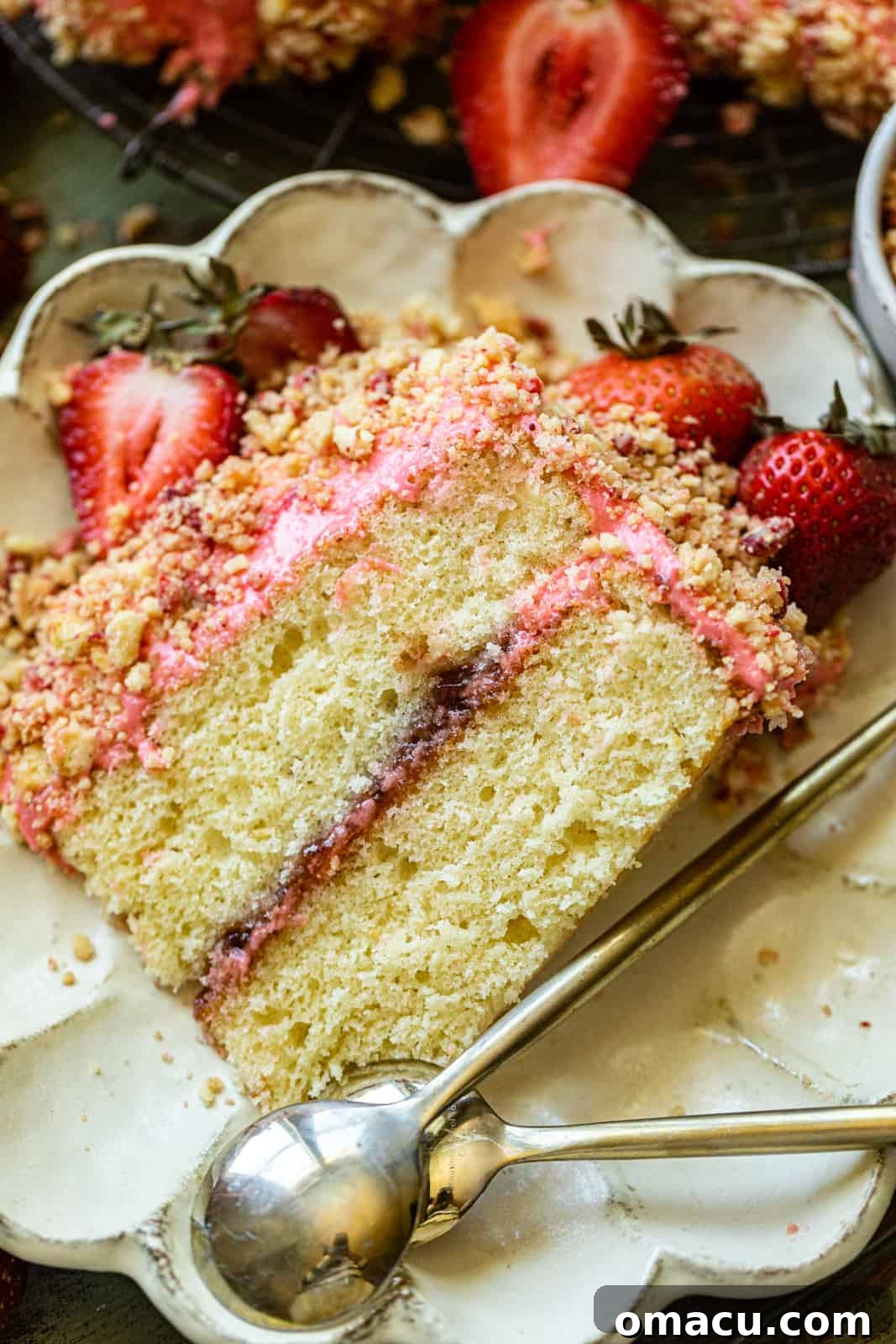 a slice of strawberry crunch cake on a plate with a spoon, showing its layers.