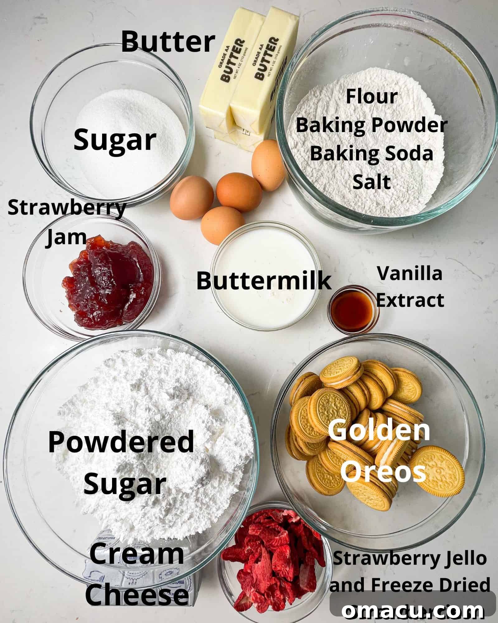 ingredients to make strawberry crunch cake - flour, baking soda, baking powder, sugar, buttermilk, golden oreos, butter, powdered sugar, strawberry jam, buttermilk, freeze dried strawberries, strawberry jello, and vanilla extract are laid out on a white surface.