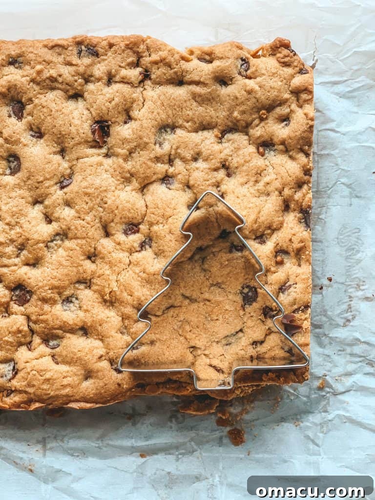Christmas tree cookie cutter pressing into a baked chocolate chip cookie bar