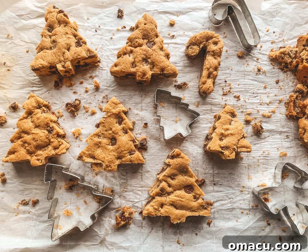 Hand cutting Christmas tree shapes from a baked cookie bar using a cookie cutter