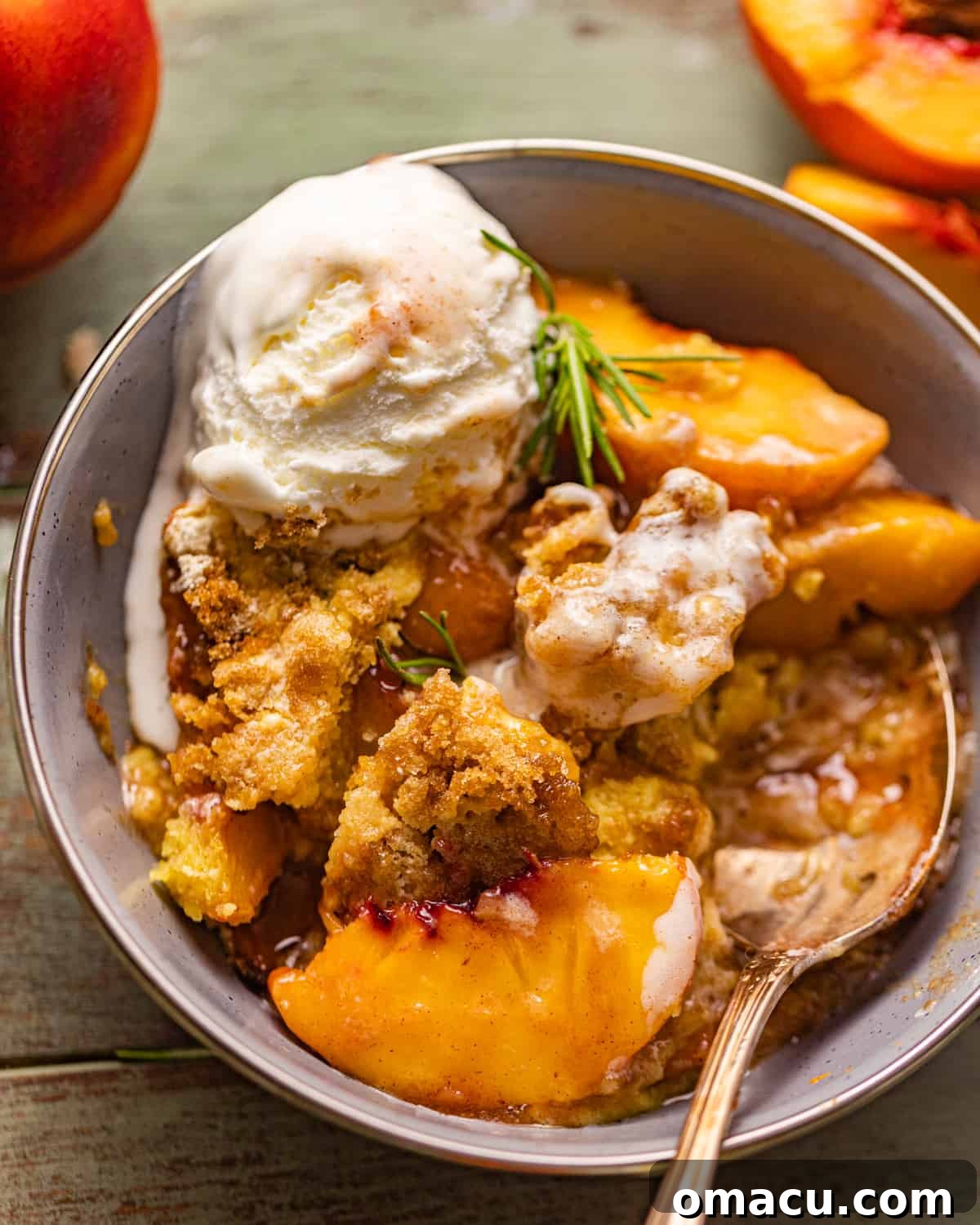 A bowl of peach cobbler with a scoop of vanilla ice cream and a spoon, ready to be enjoyed.