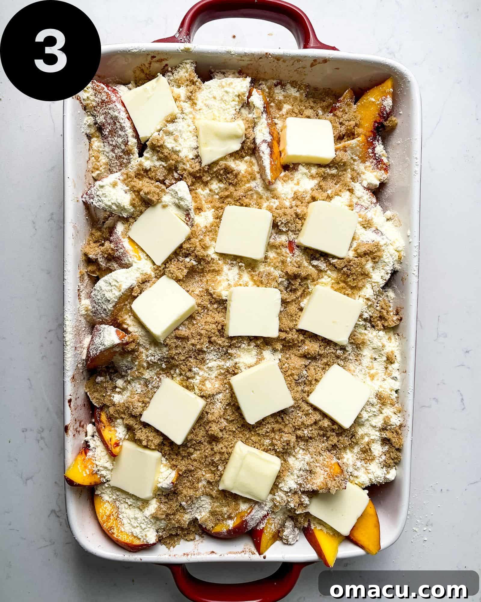 A baking dish filled with juicy peaches, completely covered with a layer of yellow cake mix, brown sugar, and pieces of butter, ready for baking.