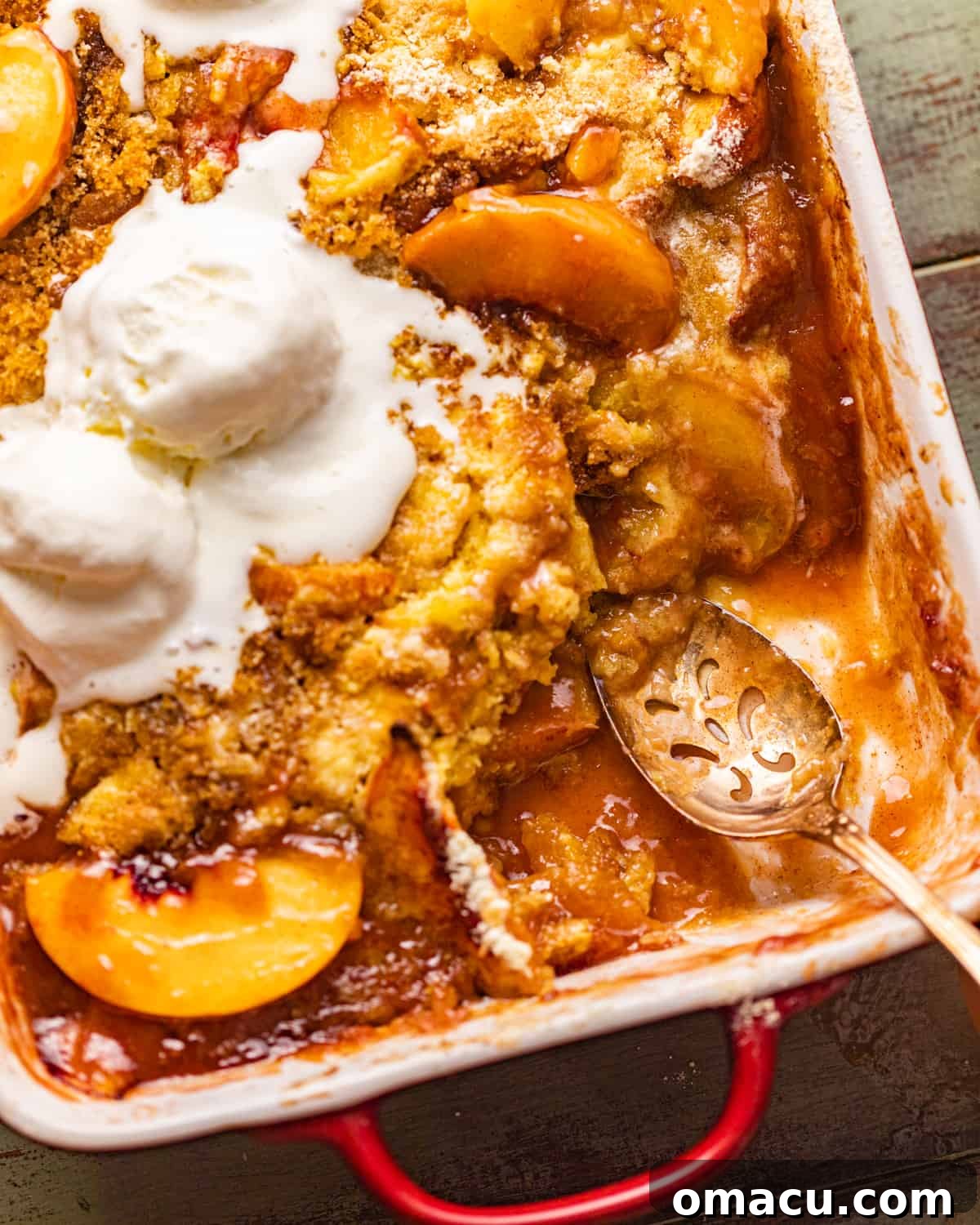 A 9x13 inch baking dish filled with freshly baked peach cobbler, with a serving spoon resting inside.