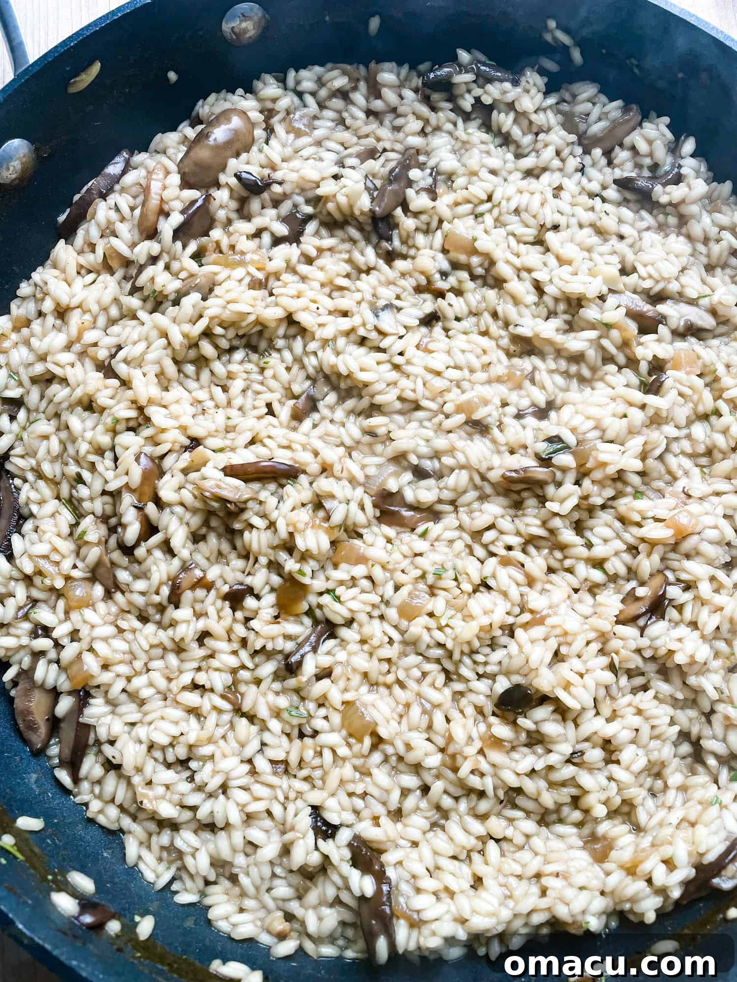 Risotto in a pan, infused with sautéed onions and garlic, simmering to a creamy consistency.