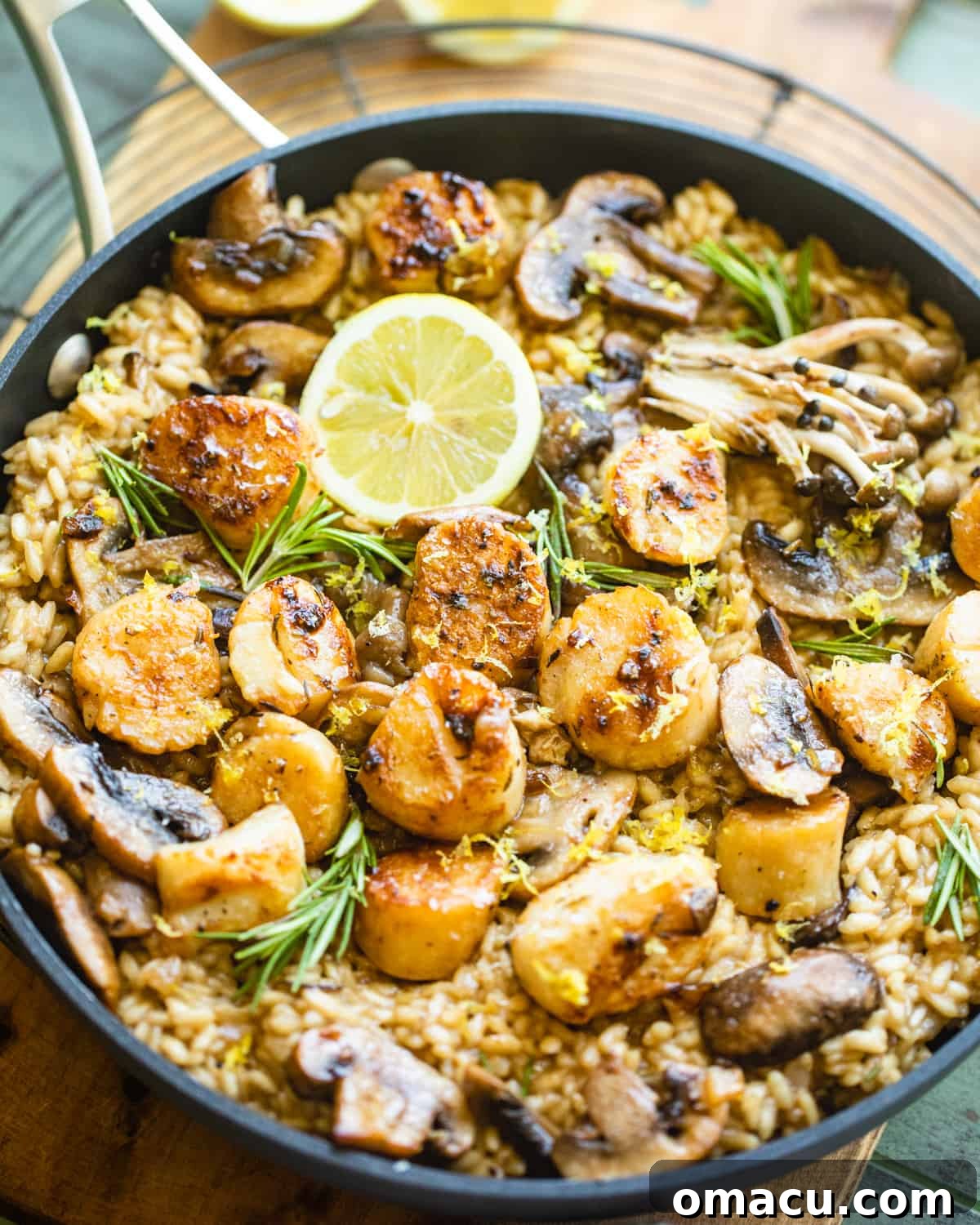 Mushroom risotto with scallops beautifully plated in a pan, garnished with fresh lemon wedges and herbs.