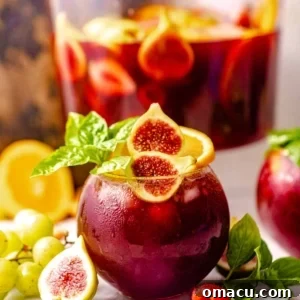 A glass of bourbon sangria in front of a pitcher of wine, glistening and ready to serve.