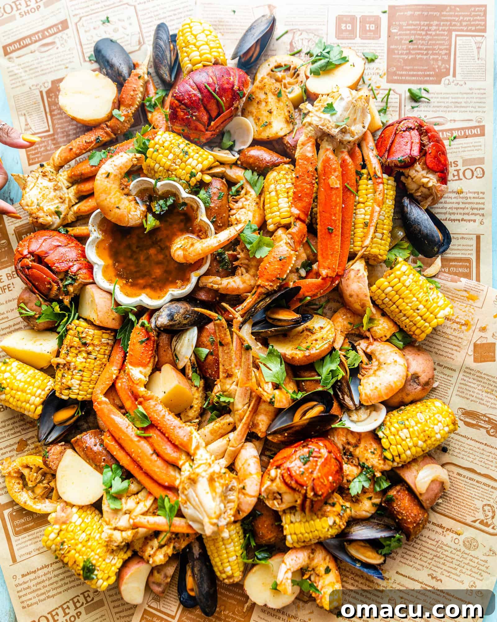 A vibrant seafood boil spread on newspaper featuring shrimp, lobster, crab legs, clams, corn on the cob, mussels, and sausages, all generously drizzled with a rich garlic butter sauce.