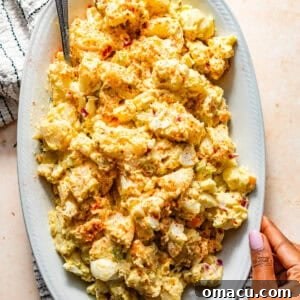 A serving plate of soul food potato salad, creamy and rich, with a hand holding the plate.