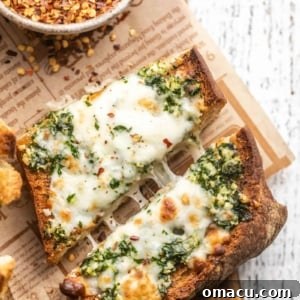 A golden-brown slice of cheesy garlic bread, cut in half and showing off its melted cheese and herbaceous crust.