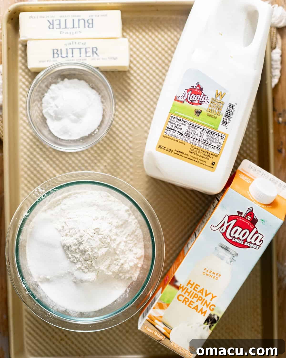 Ingredients laid out for buttermilk biscuits: buttermilk, heavy cream, all-purpose flour, cake flour, baking powder, baking soda, salted butter, sugar, kosher salt, and an egg.