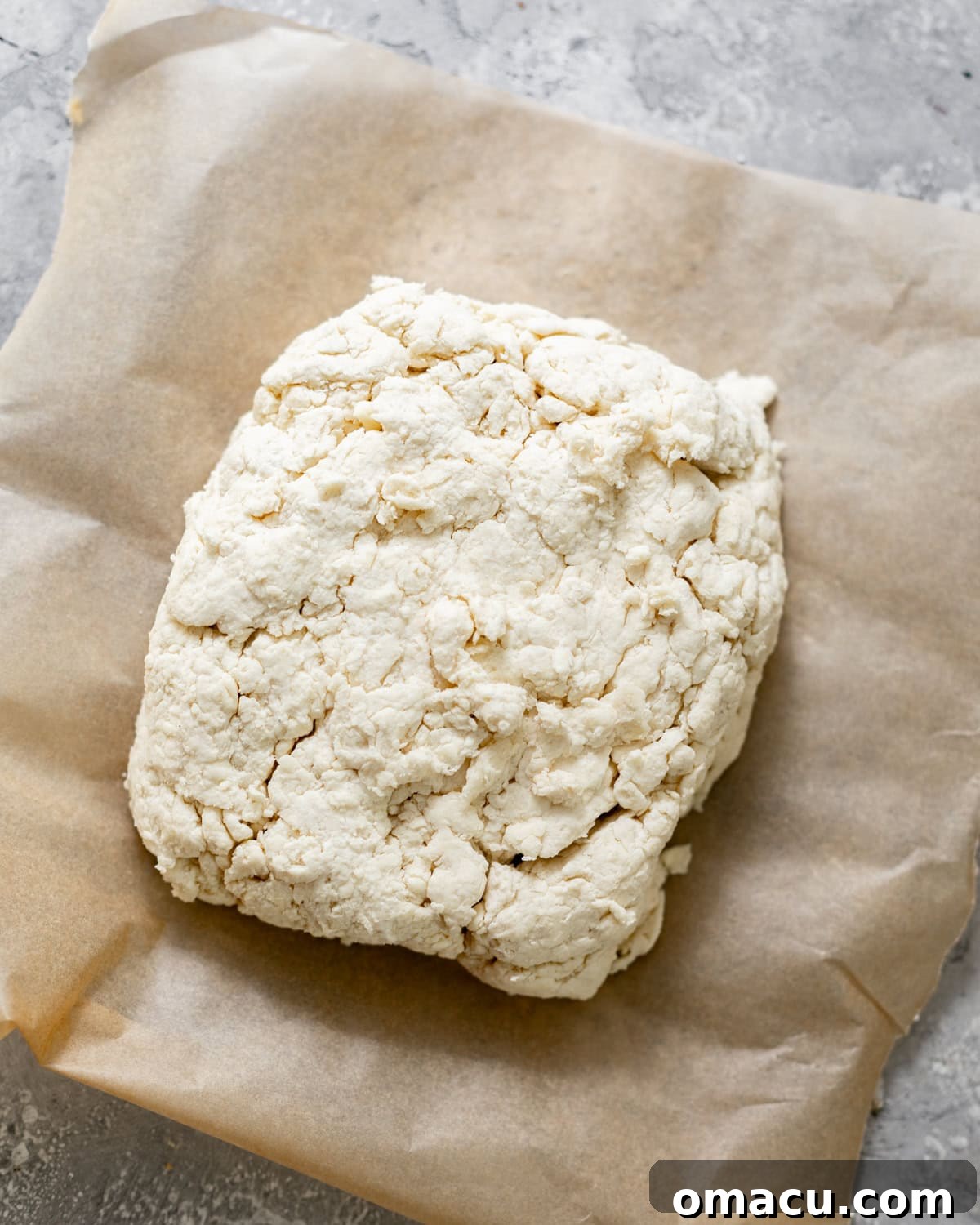 Shaggy biscuit dough pressed into a rectangle on a piece of parchment paper.