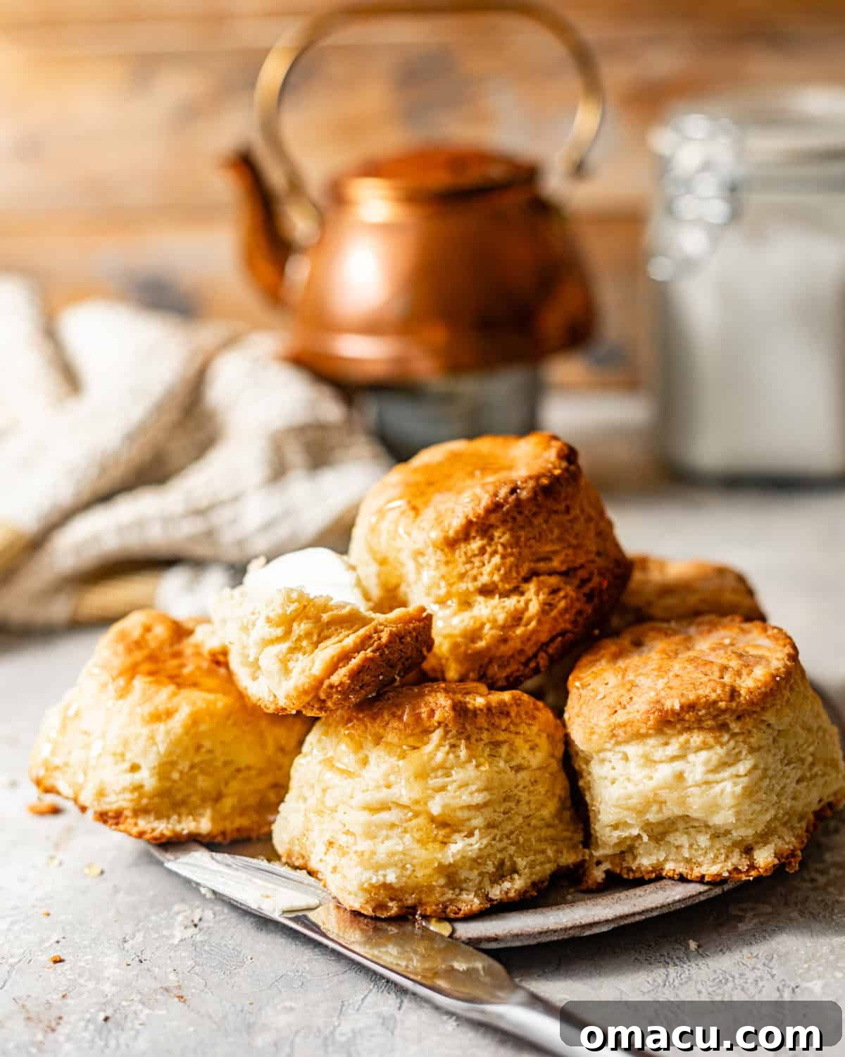 Freshly baked buttermilk biscuits on a plate with a butter knife, ready to be served.