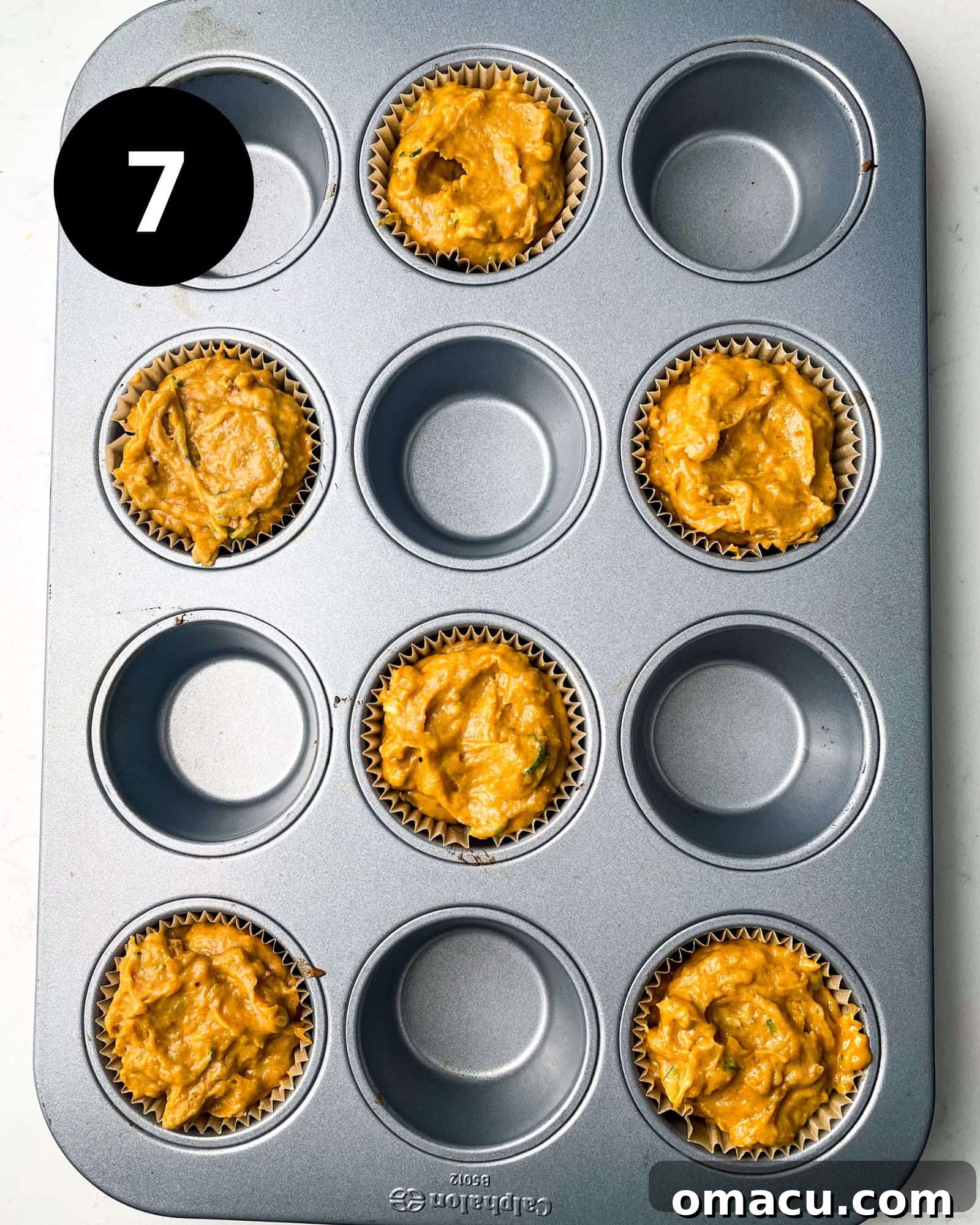 A muffin pan with liners filled with golden-hued muffin batter, ready for baking.