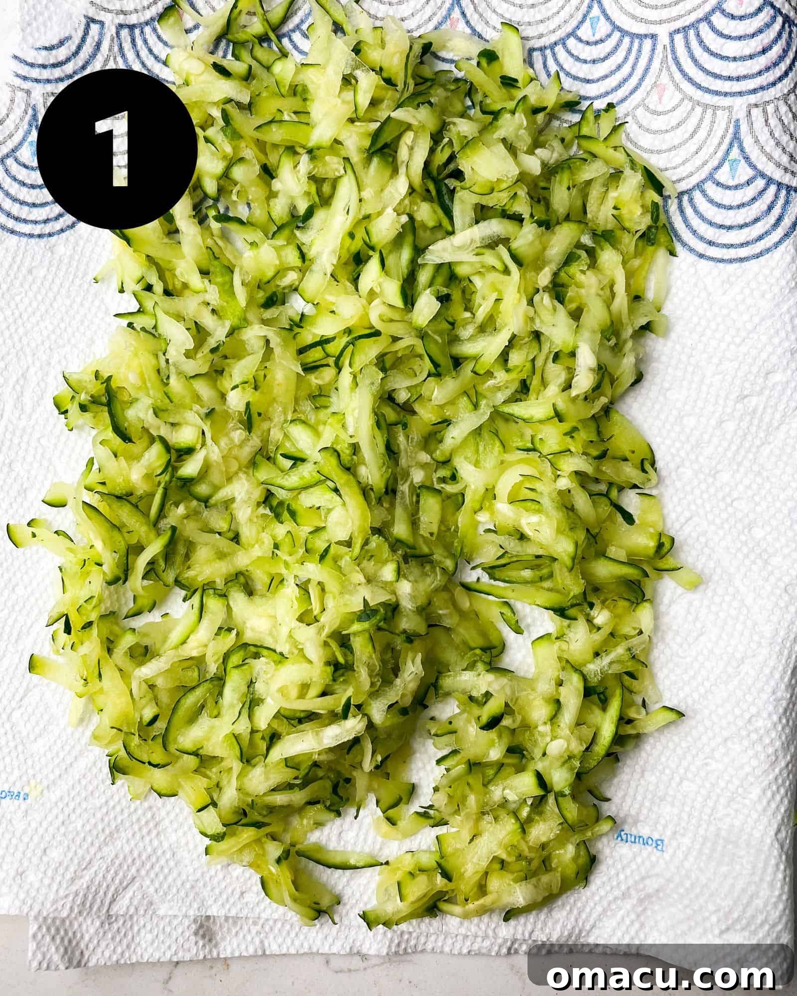 Freshly grated zucchini sitting on a paper towel, ready to be squeezed of excess moisture for baking.