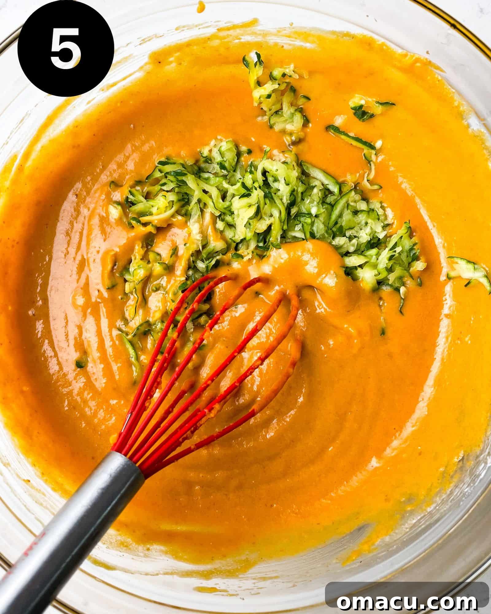 Delicious pumpkin muffin batter in a bowl, with visible flecks of grated zucchini mixed in.