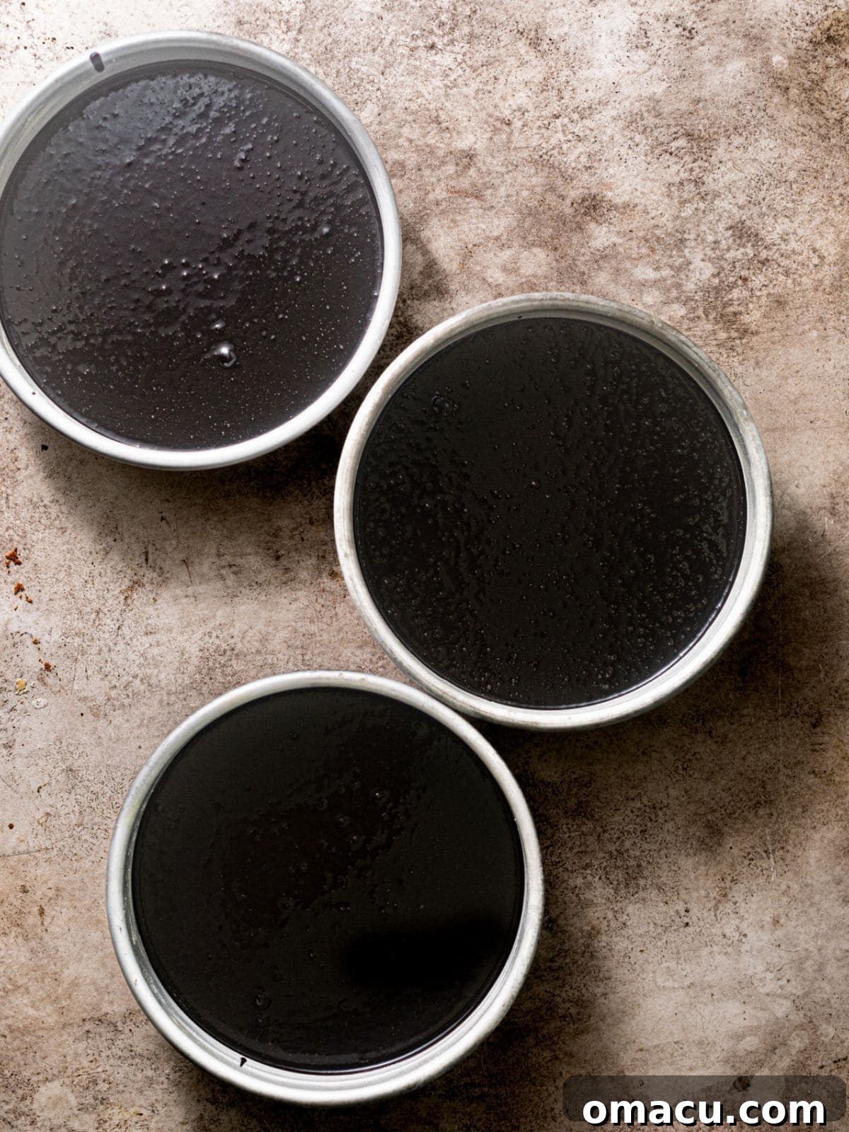 Black velvet cake batter evenly divided into three 8-inch round cake pans, ready for baking.