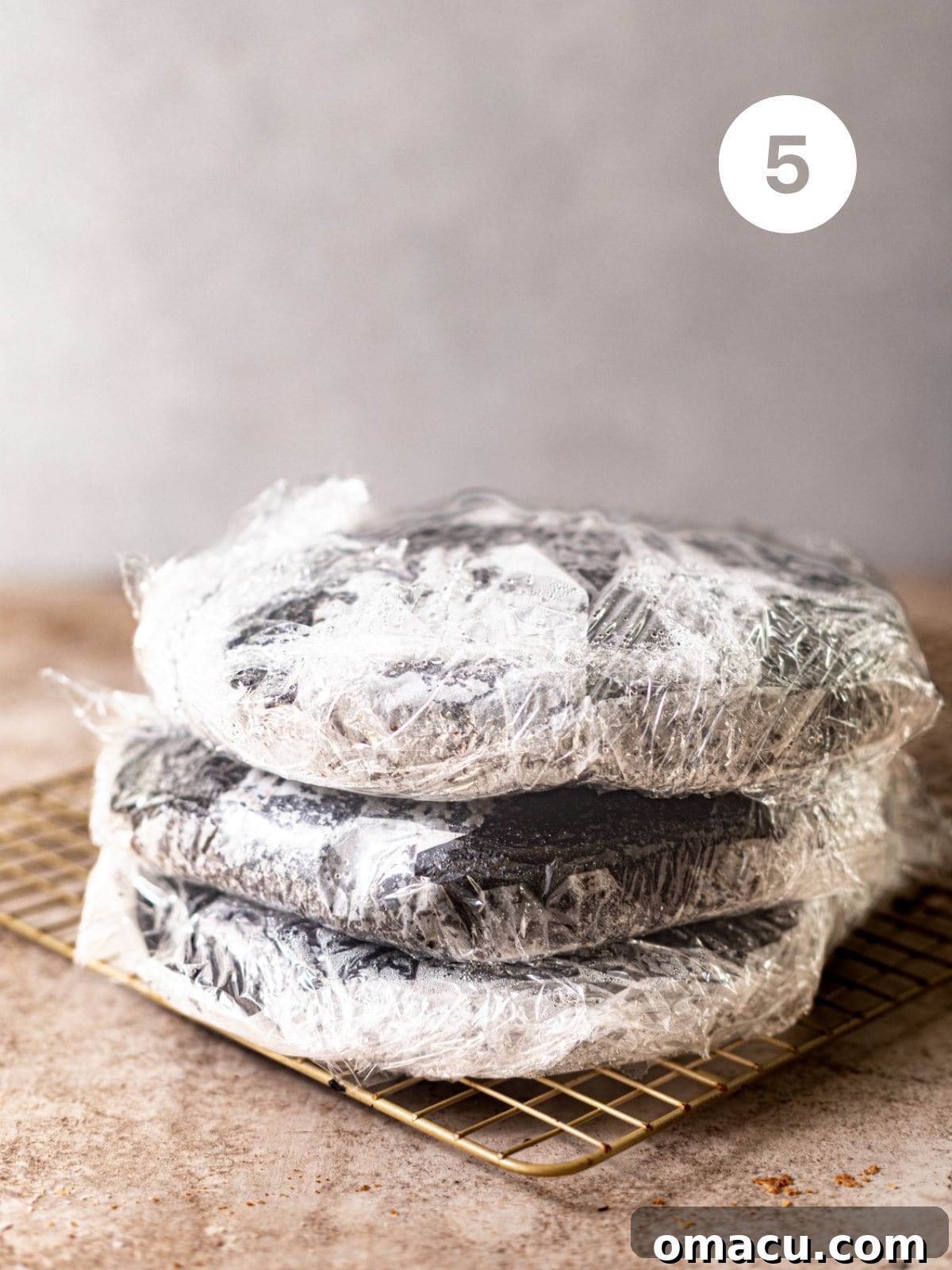 Warm, freshly baked cake layers carefully wrapped in plastic wrap to cool and retain moisture.