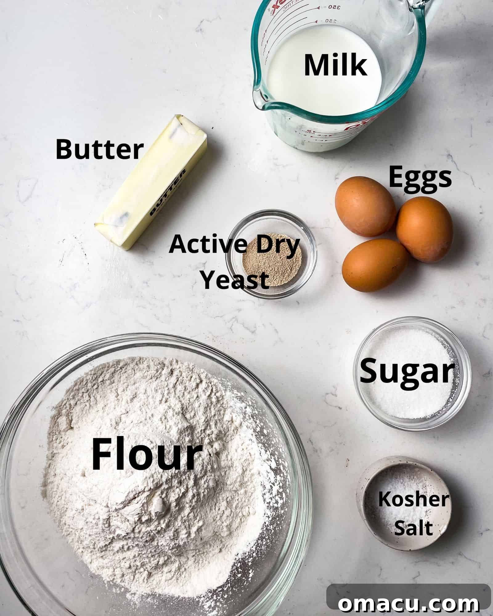 Ingredients for making brioche dinner rolls, including flour, sugar, active dry yeast, butter, milk, and eggs, neatly arranged.