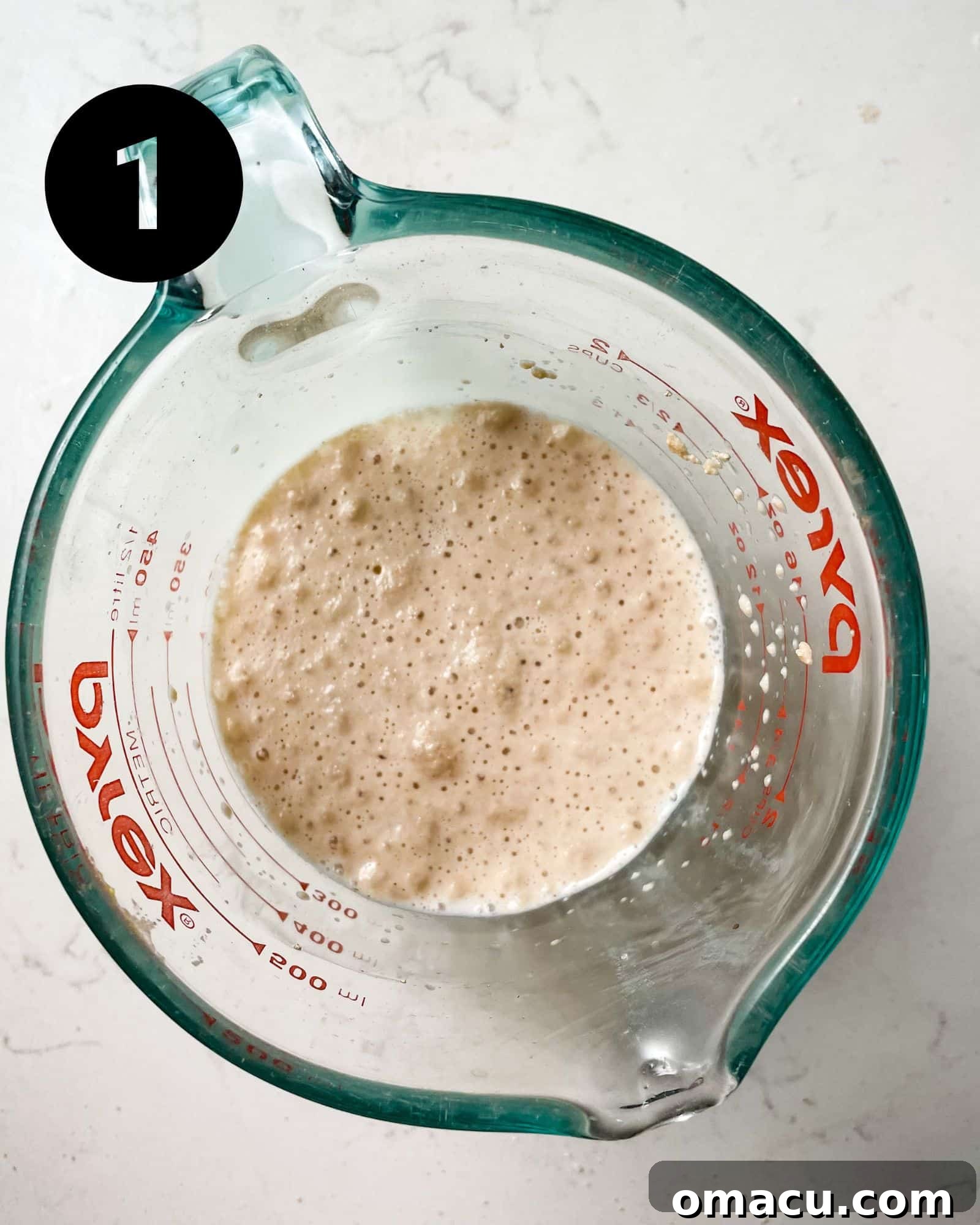 Active dry yeast and warm milk combined in a measuring glass, showing the blooming process.