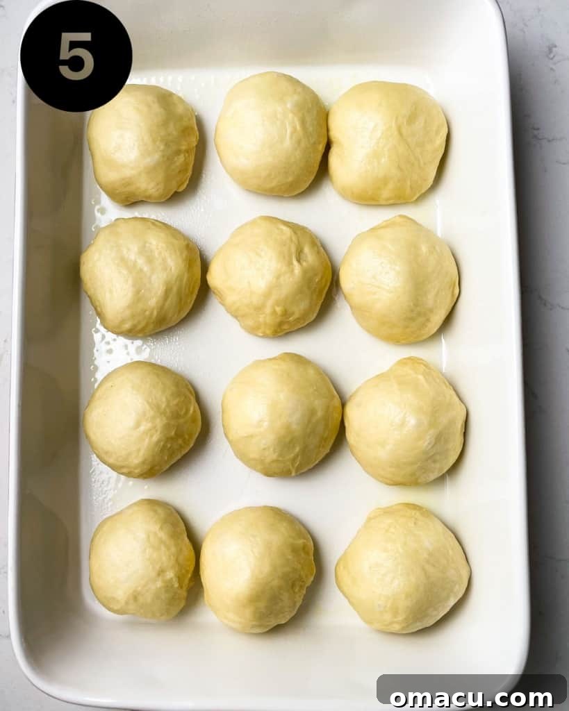 Brioche dinner rolls arranged in a baking dish, undergoing their second rise.