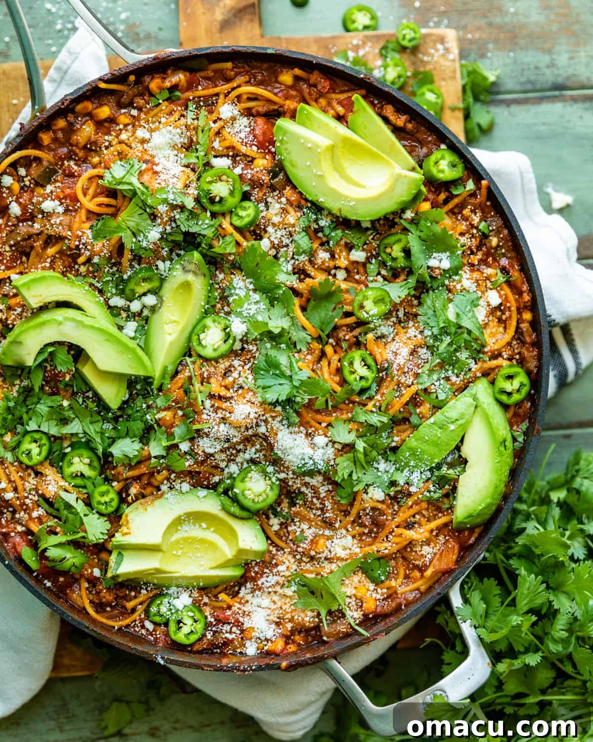 Mexican spaghetti in a large skillet garnished with cotija, avocado, and cilantro, ready to be served.
