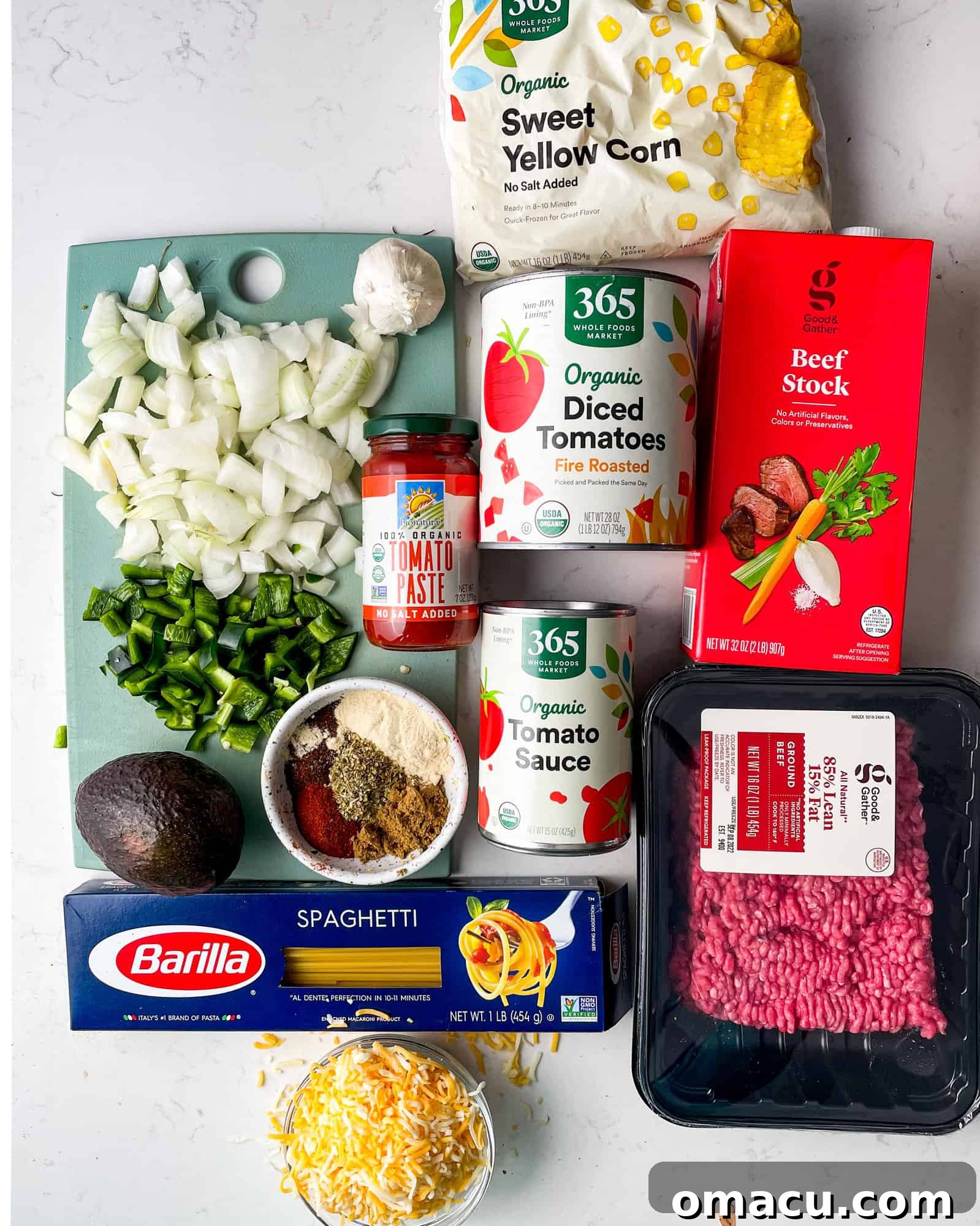 Ingredients laid out for Mexican spaghetti: ground beef, various tomatoes, onions, poblano pepper, garlic, corn, beef broth, spaghetti, cheese, and taco seasoning.