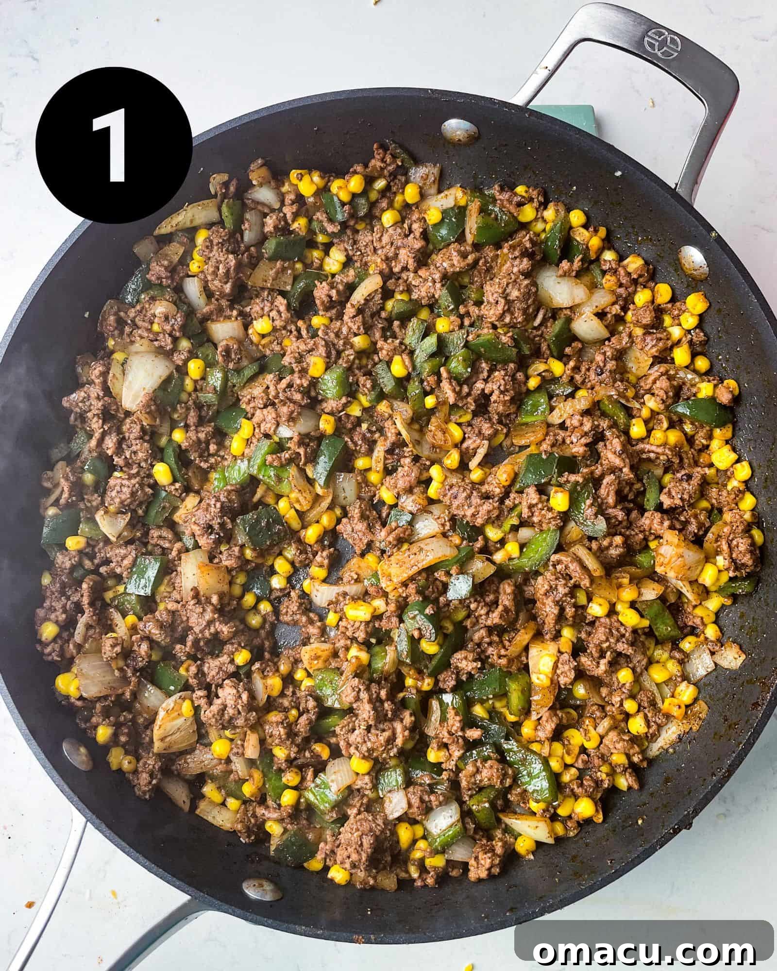 Ground beef, onions, peppers, corn, and seasonings cooking together in a large pan, forming the base of the Mexican spaghetti.