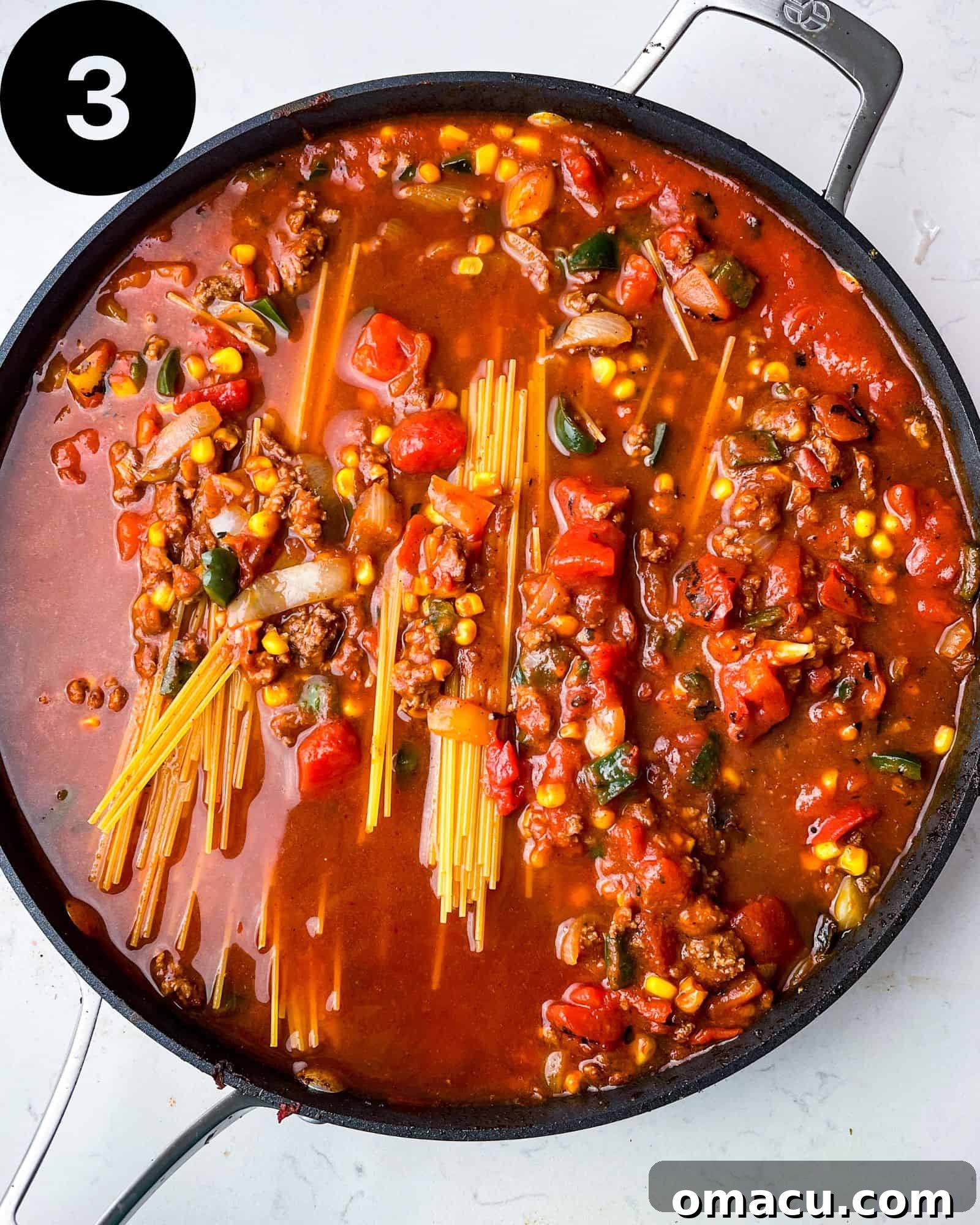 Cooked spaghetti in a pan with meat, corn, and peppers, topped with melted cheese.