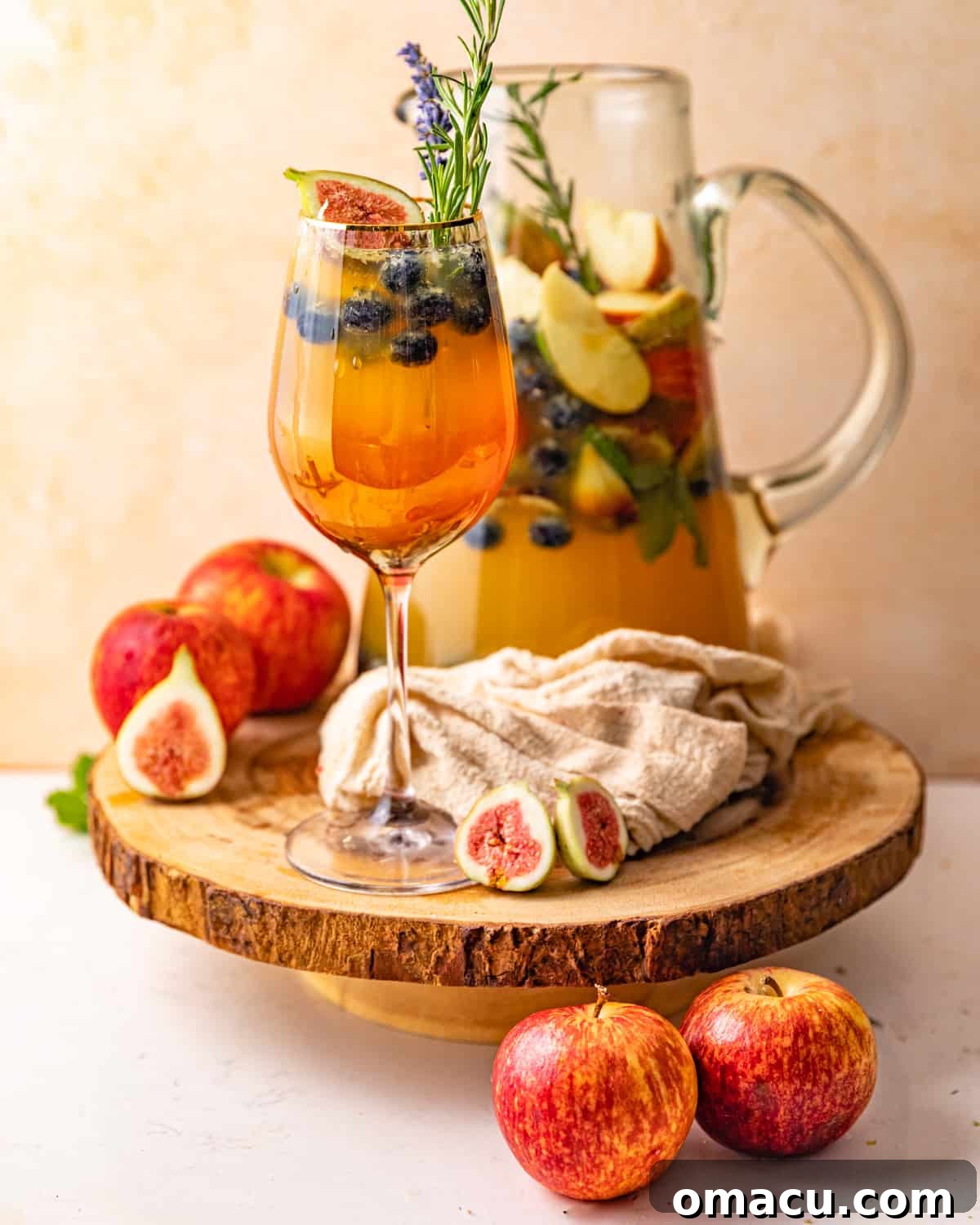 A beautifully presented glass of white wine sangria in front of a large pitcher, garnished with fresh fruit and herbs.