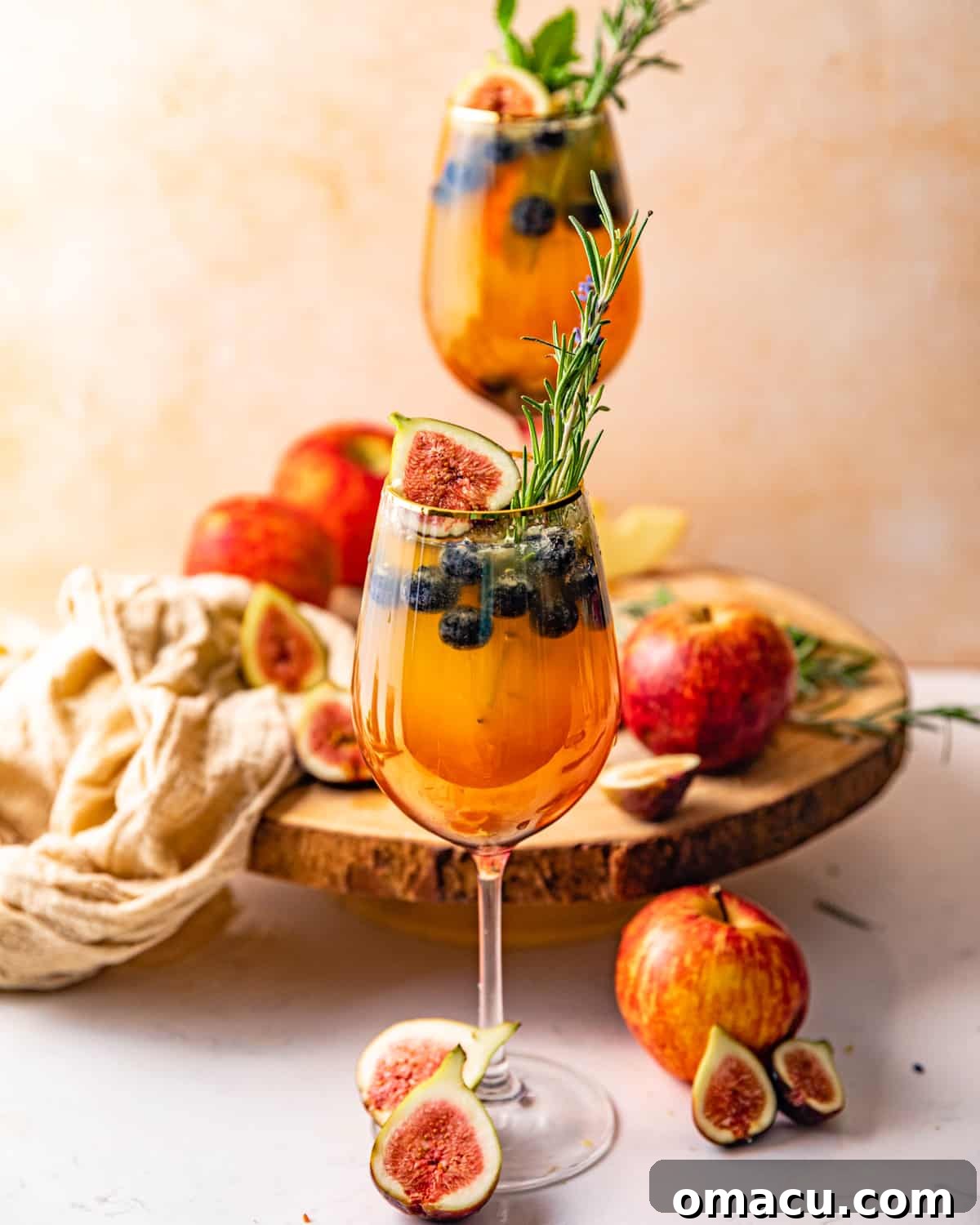 Two elegant glasses of white wine sangria, exquisitely garnished with fresh herbs, sliced figs, and crisp apple wedges.