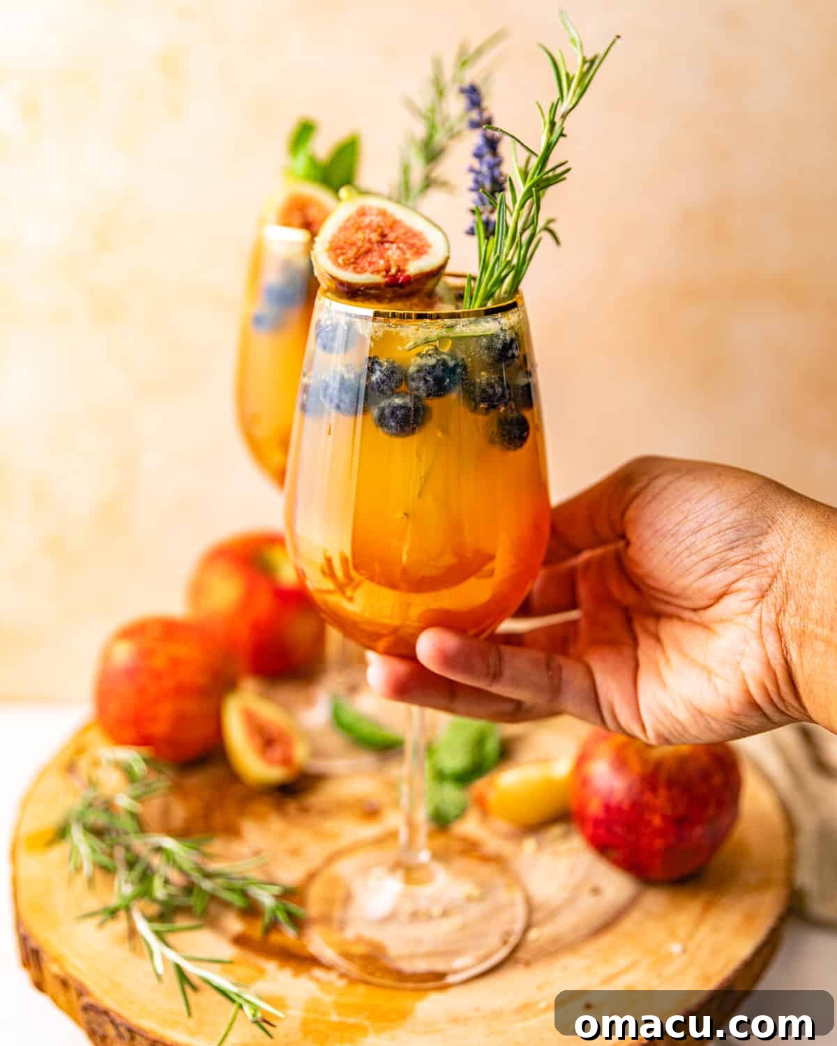 A hand gracefully holding a glass of refreshing white wine sangria, showing off its beautiful contents.