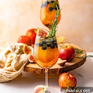 Two glasses of sangria garnished with fresh herbs, figs, and apples.