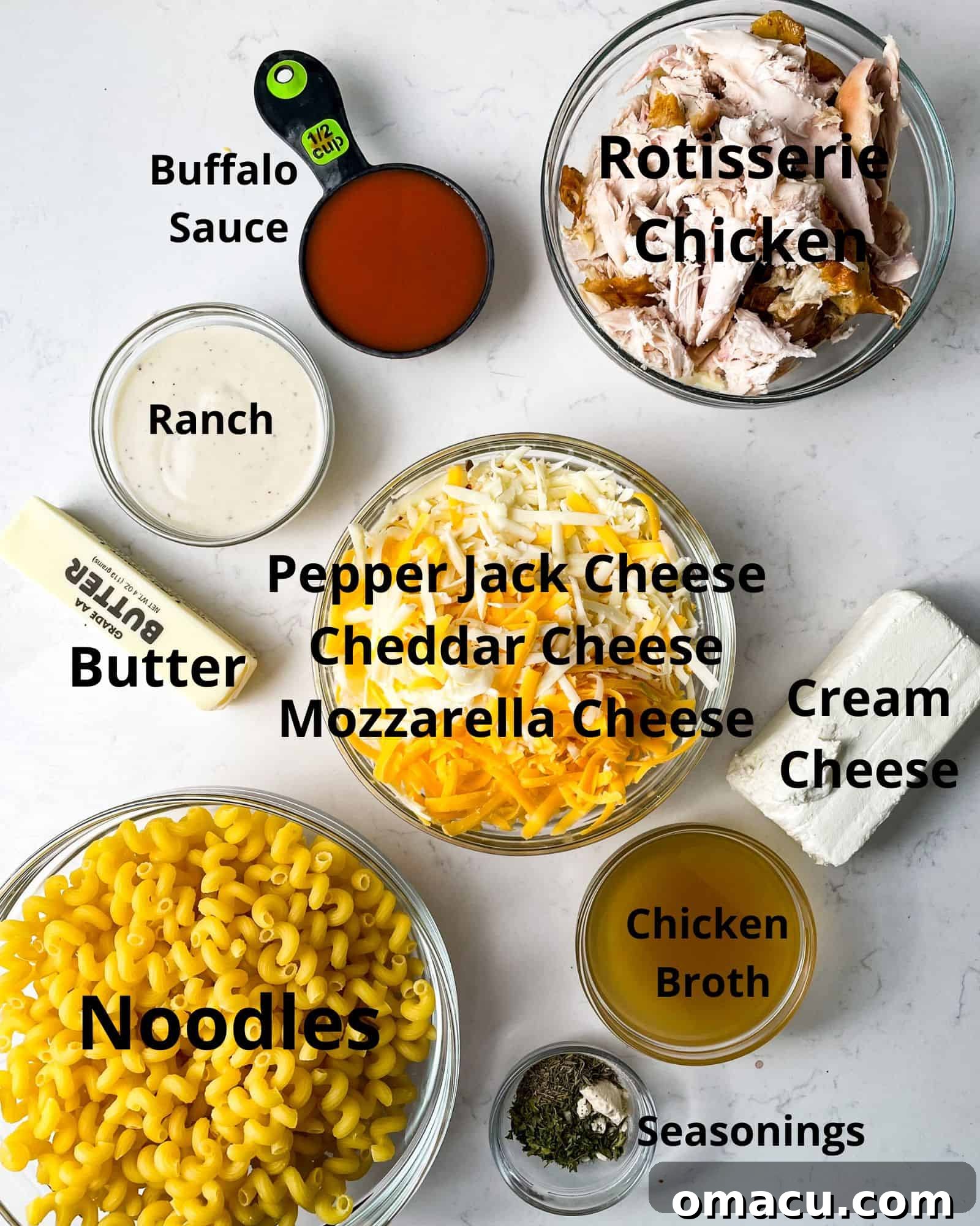 Arrangement of ingredients for buffalo mac and cheese: shredded chicken, various cheeses, buffalo sauce, ranch dressing, butter, milk, chicken broth, pasta, and seasonings.