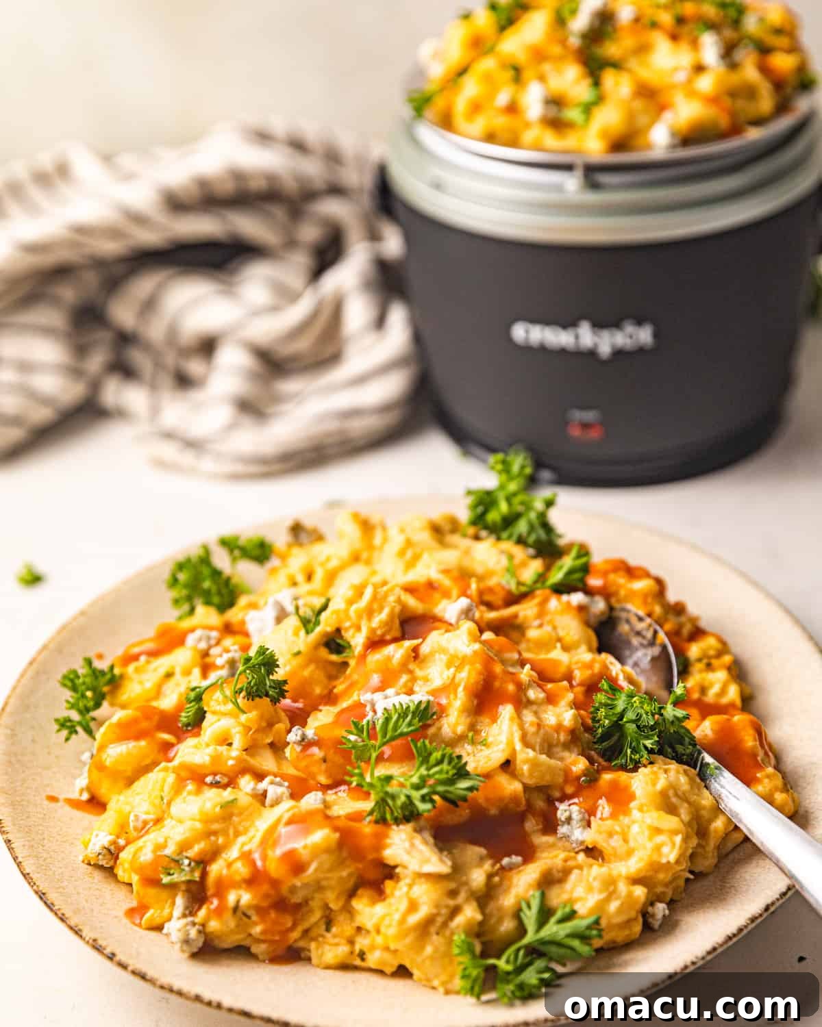 Finished Crockpot Buffalo Chicken Mac and Cheese served on a white plate with a fork, garnished with green onions.