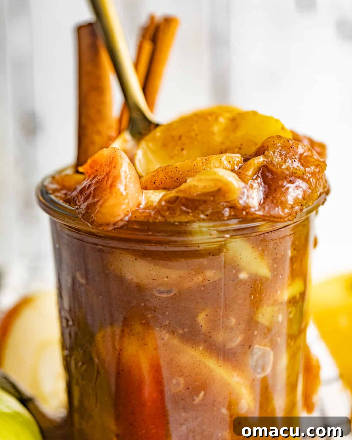Up-close photo of rich, spiced apple pie filling in a glass jar, garnished with cinnamon sticks.