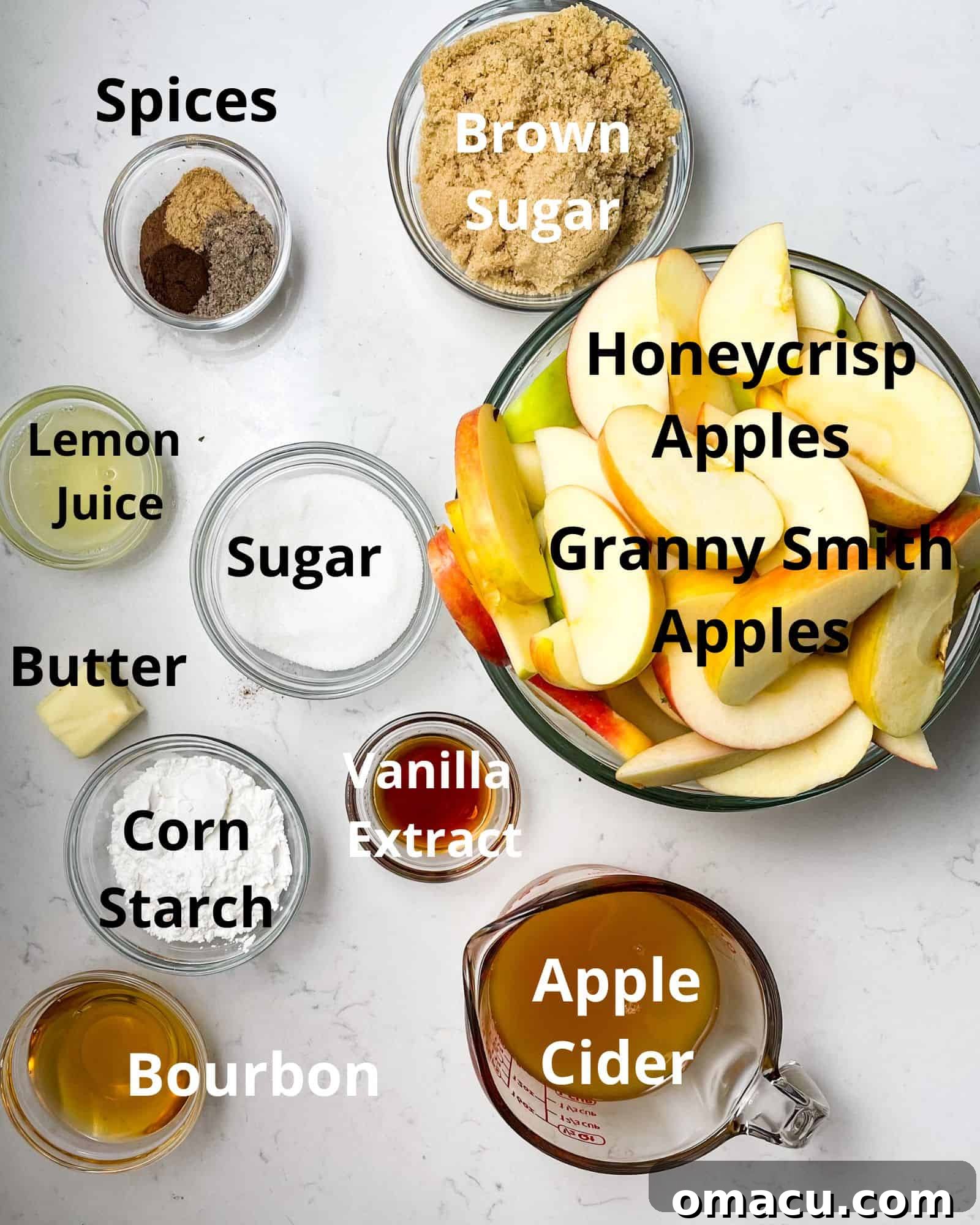 Ingredients laid out for apple pie filling: fresh apples, apple cider, bourbon, cornstarch, sugars (brown and white), spices, vanilla extract, butter, and lemon juice.