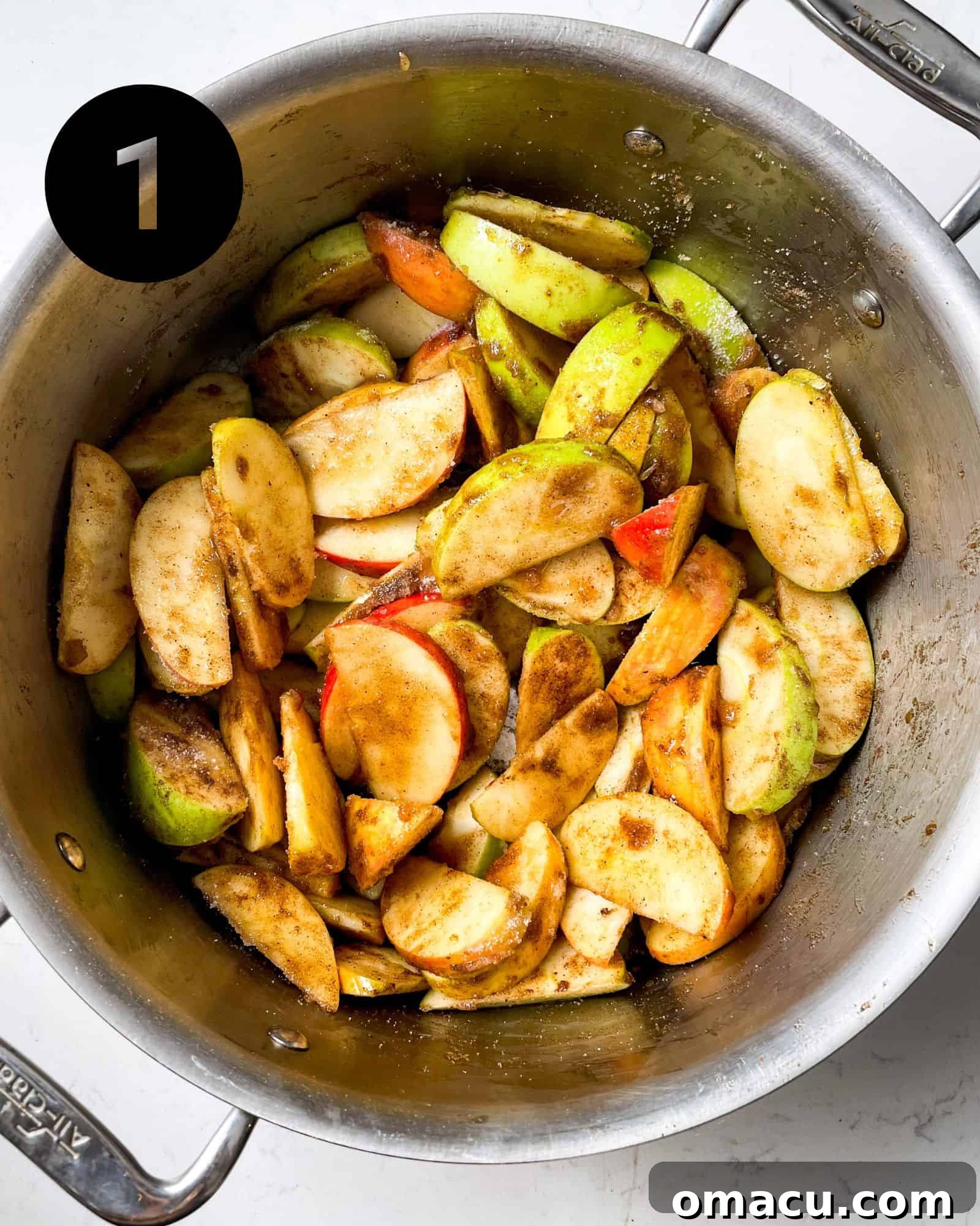 Sliced apples mixed with sugars and spices resting in a large pot, ready for cooking.