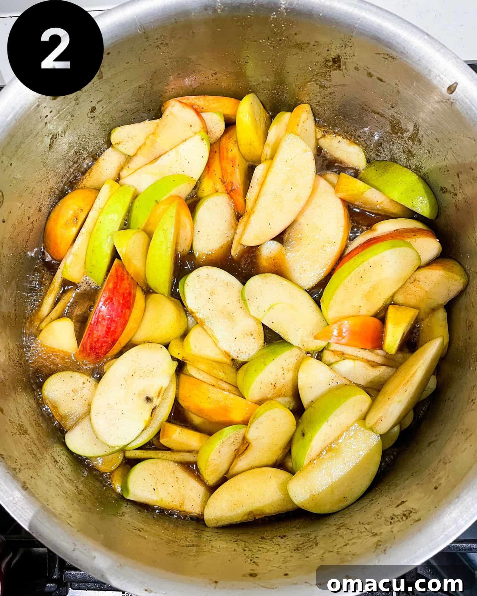 Apples cooking in a large pot on the stove, simmering in their spiced liquid.