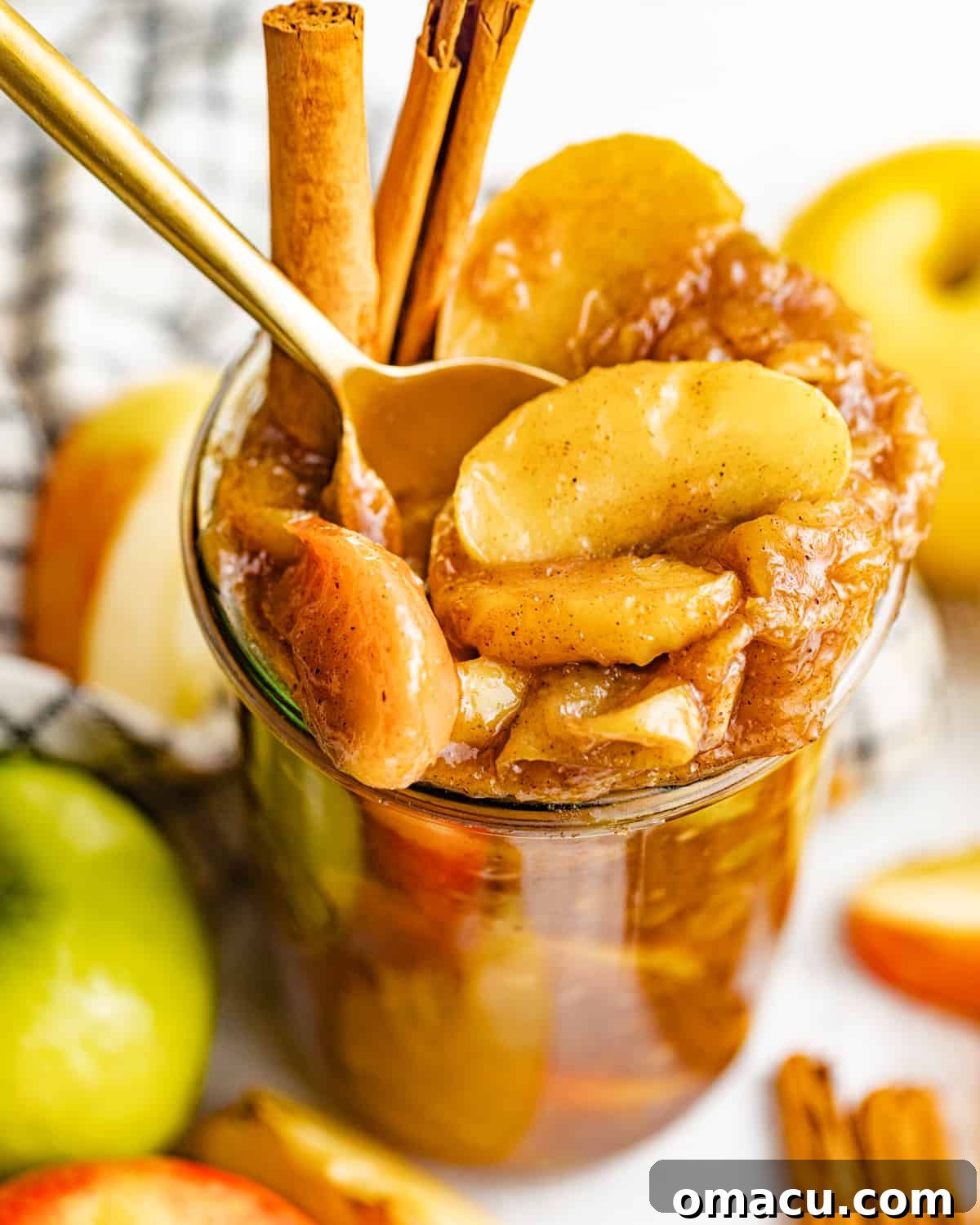 An up-close photo of rich homemade apple pie filling in a glass jar, with a spoon resting inside, ready to be served.