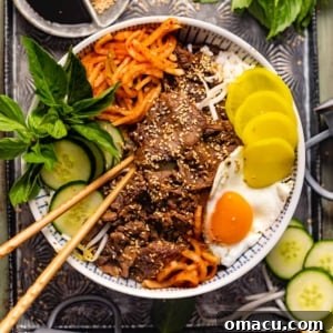 Korean Bulgogi in a bowl with rice, cucumbers, a fried egg, and kimchi.