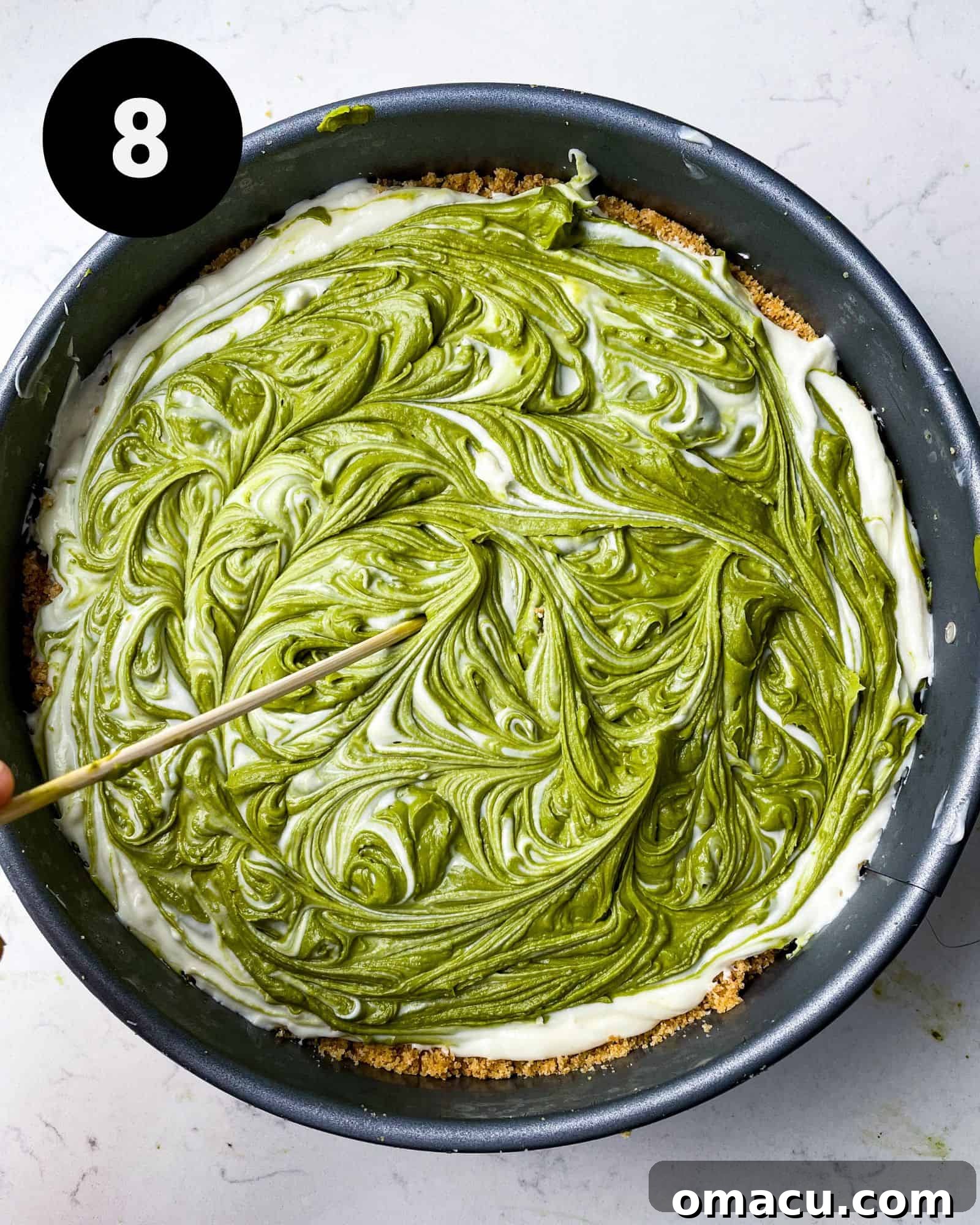 The assembled matcha and white chocolate cheesecake chilling in the pan, showing off its beautiful swirl.