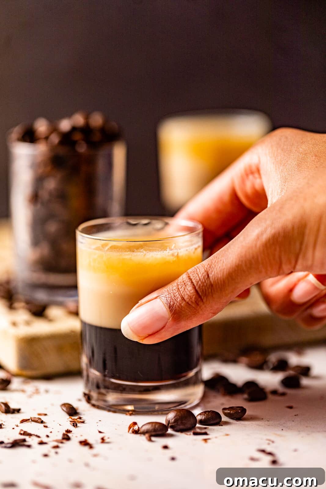 A hand gently holding a shot glass containing a beautiful, freshly made Duck Fart Shot.