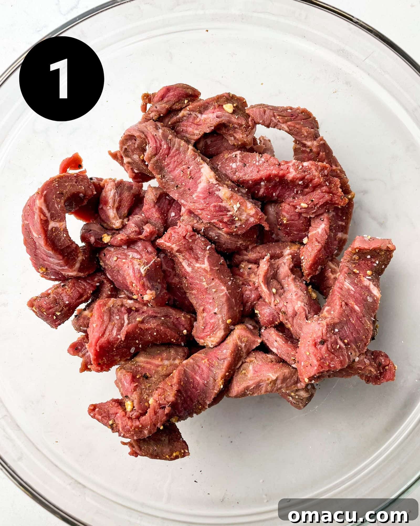 Thinly sliced sirloin steak seasoned with spices in a bowl.