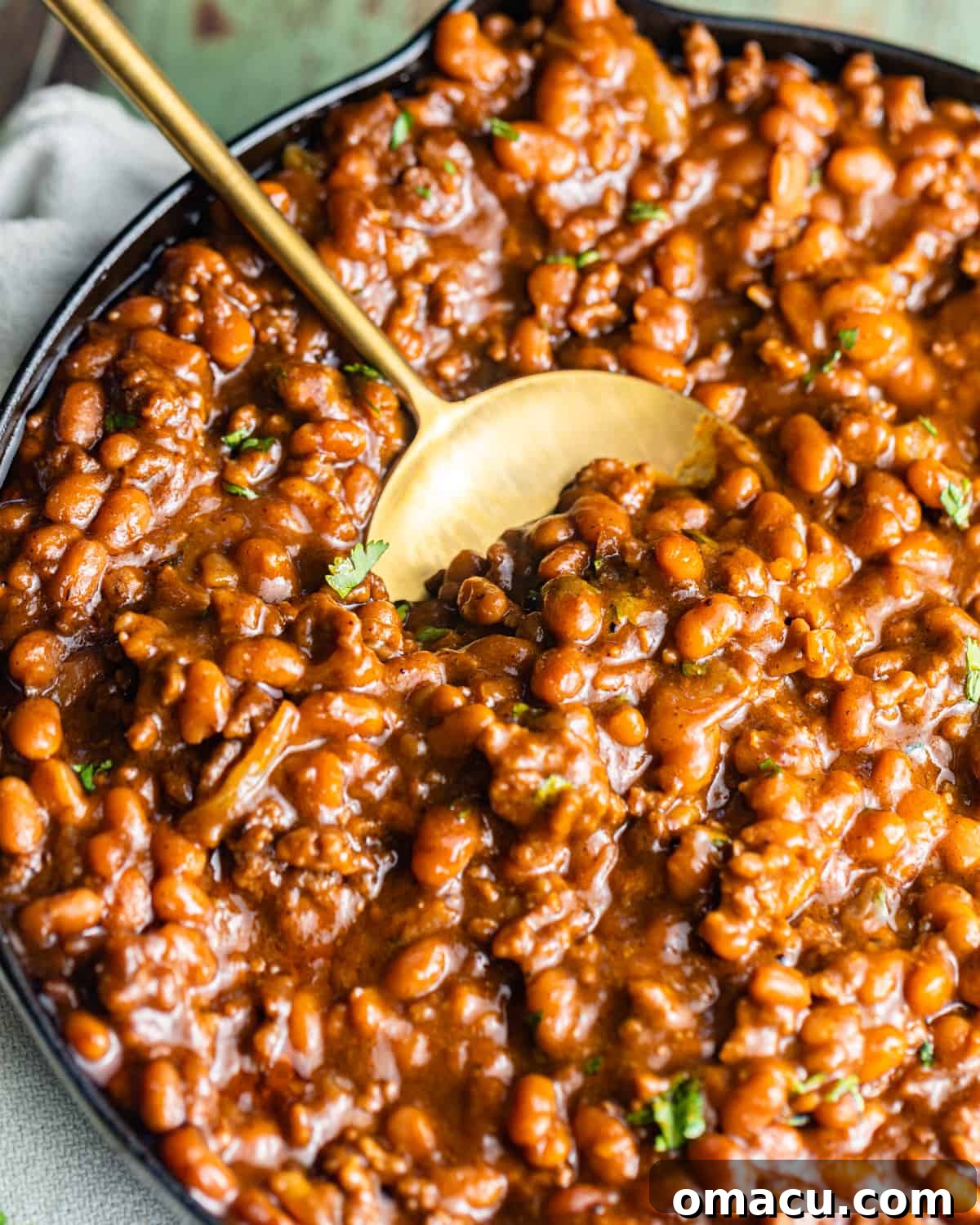 close up photo of a spoon in a pot of baked beans, showing the thick, savory sauce.