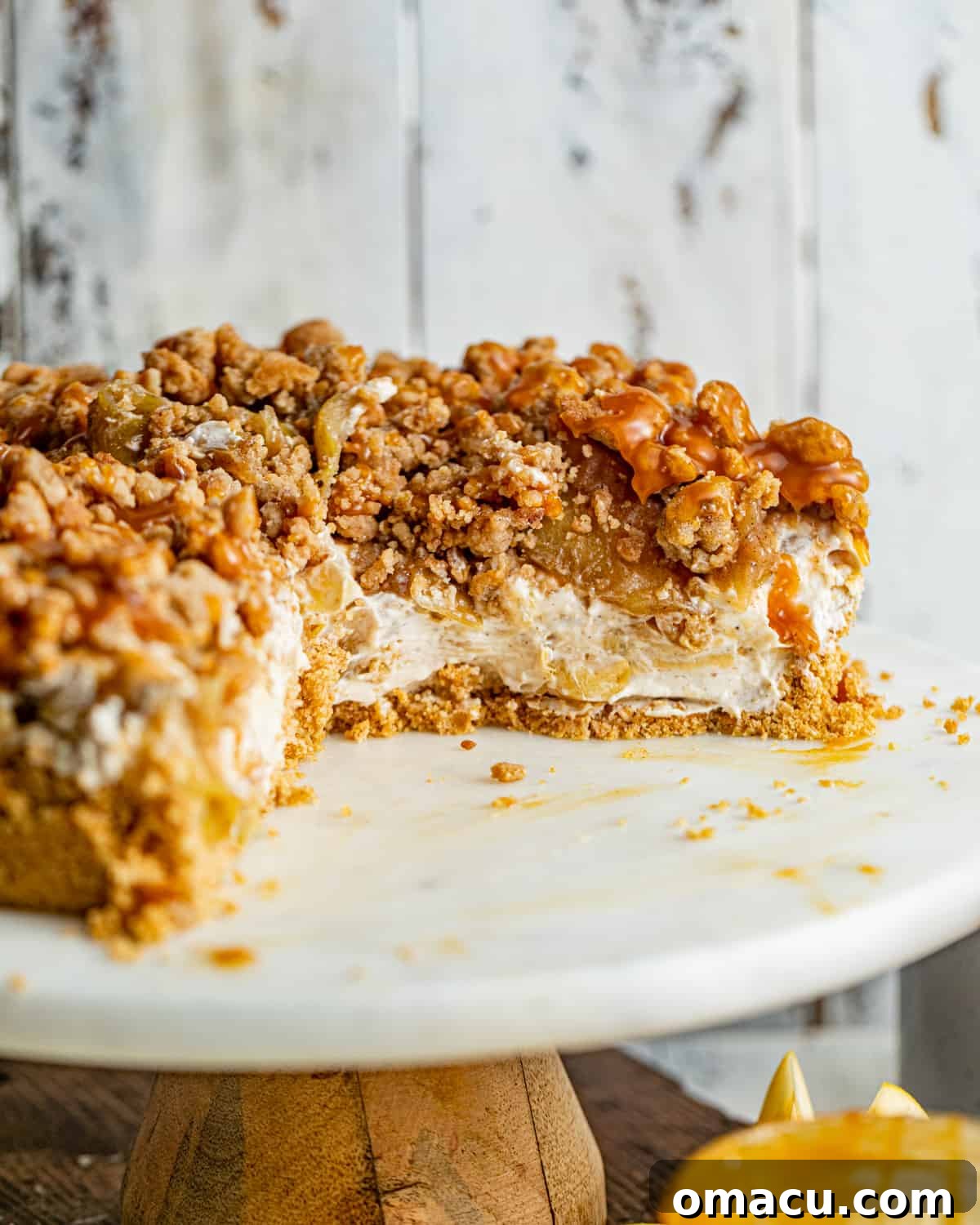 A half-cut Apple Pie Stuffed Cheesecake, beautifully drizzled with sweet caramel sauce, showcasing its distinct layers of graham cracker crust, creamy cheesecake, and chunky apple pie filling.