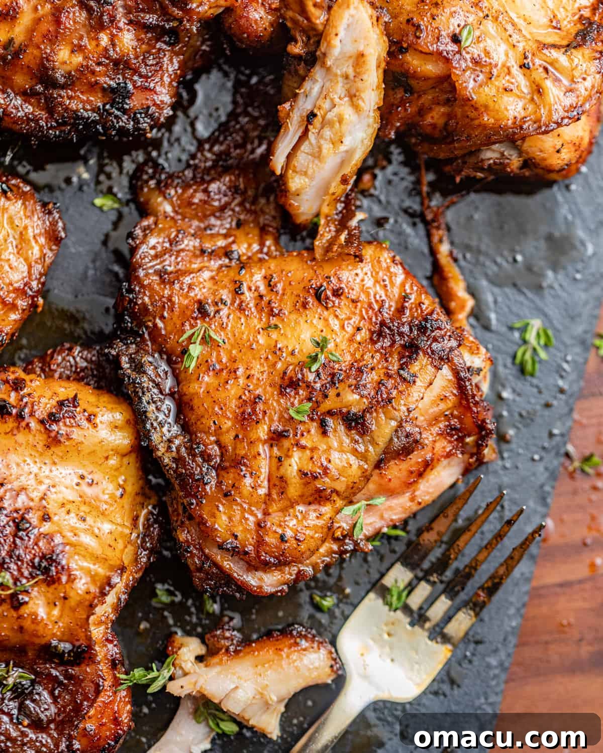 smoked chicken thighs on a plate with a fork and fresh herbs.