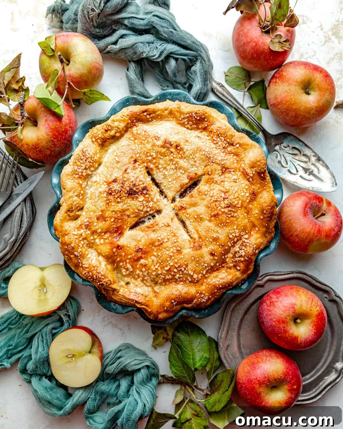 A beautifully baked maple apple pie in a rustic pie dish, surrounded by fresh red and green apples, signifying the perfect fall harvest dessert.