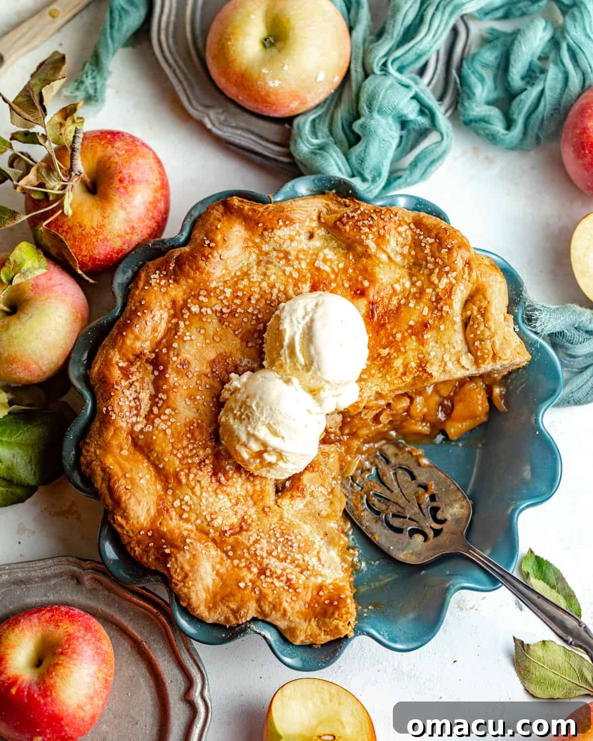 A whole maple apple pie in a rustic pie plate, freshly baked and ready to be sliced, with a scoop of melting vanilla ice cream nearby.