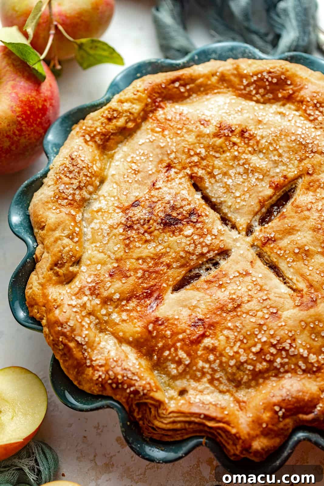 A freshly baked maple apple pie in a ceramic pie dish, showcasing its golden, crimped crust and alluring aroma.